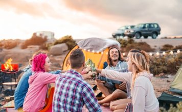Happy friends toasting beers at barbecue camping party