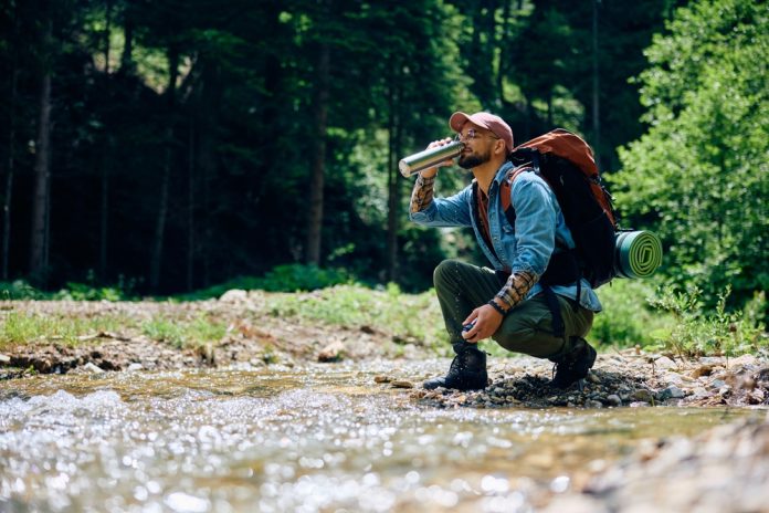 Hiker drinking water from a stream from his water bottle