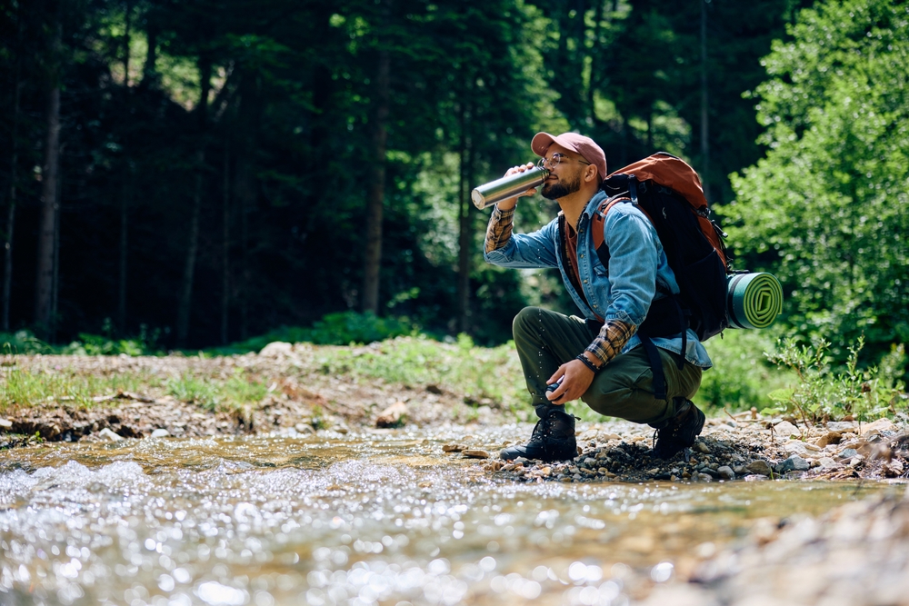 Hiker drinking water from a stream from his water bottle