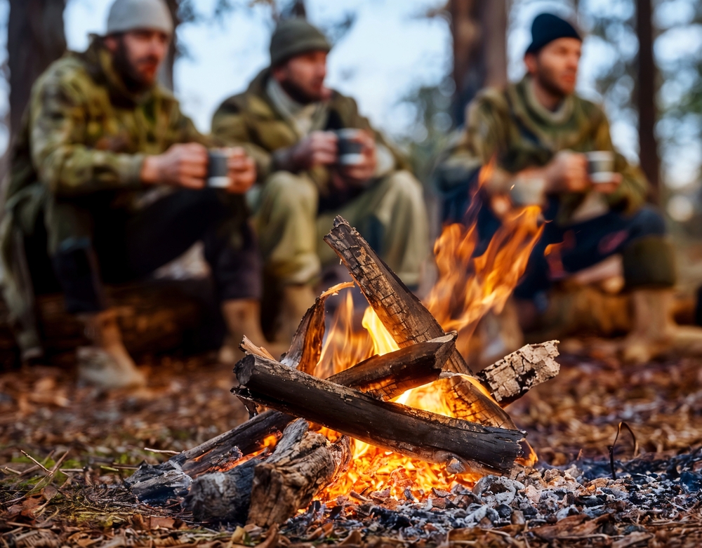 Three hunters in winter gear sit around a campfire in the forest