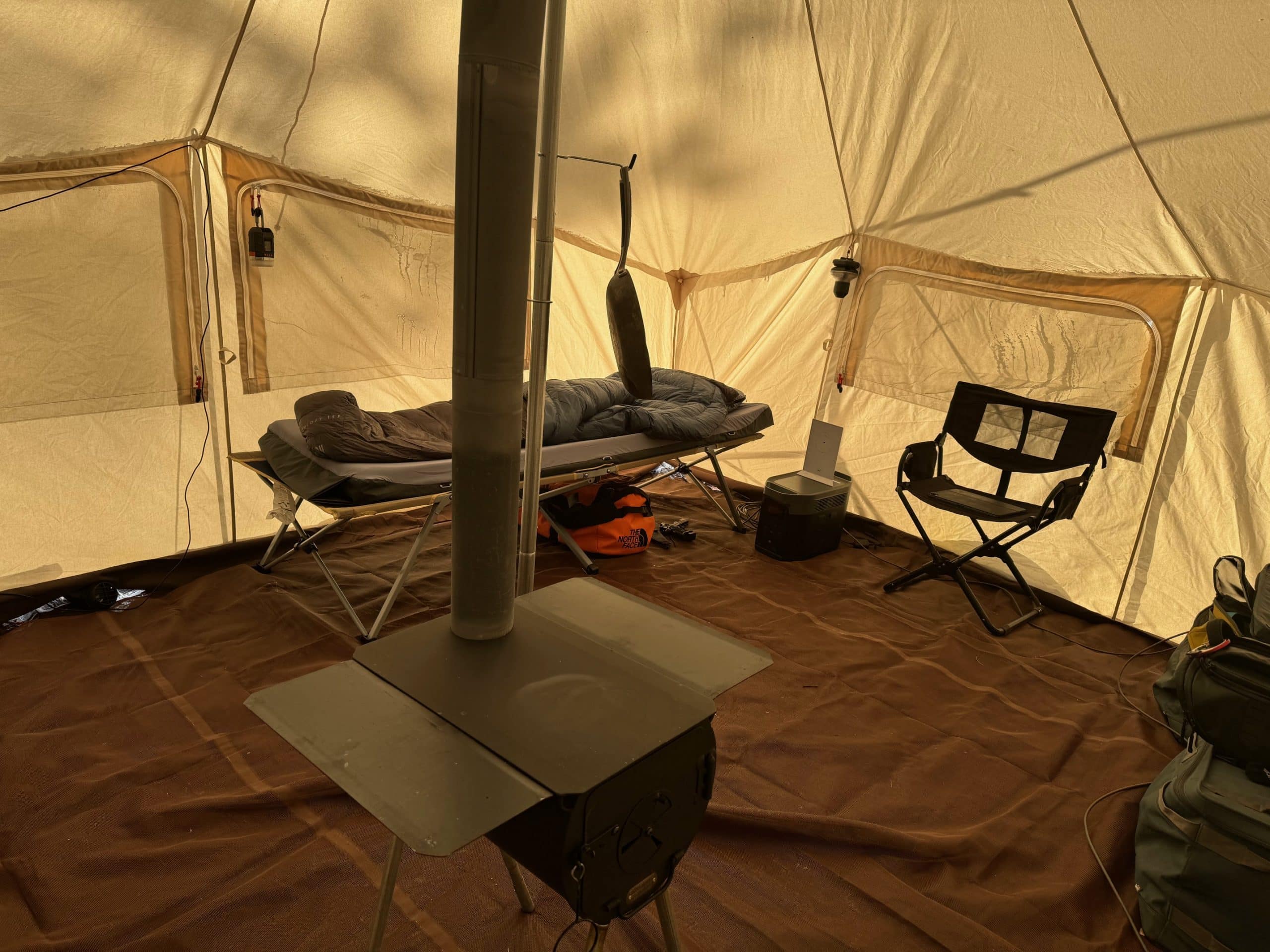 A Hest mattress on top of a cot in a canvas wall tent with a wood stove in the center 