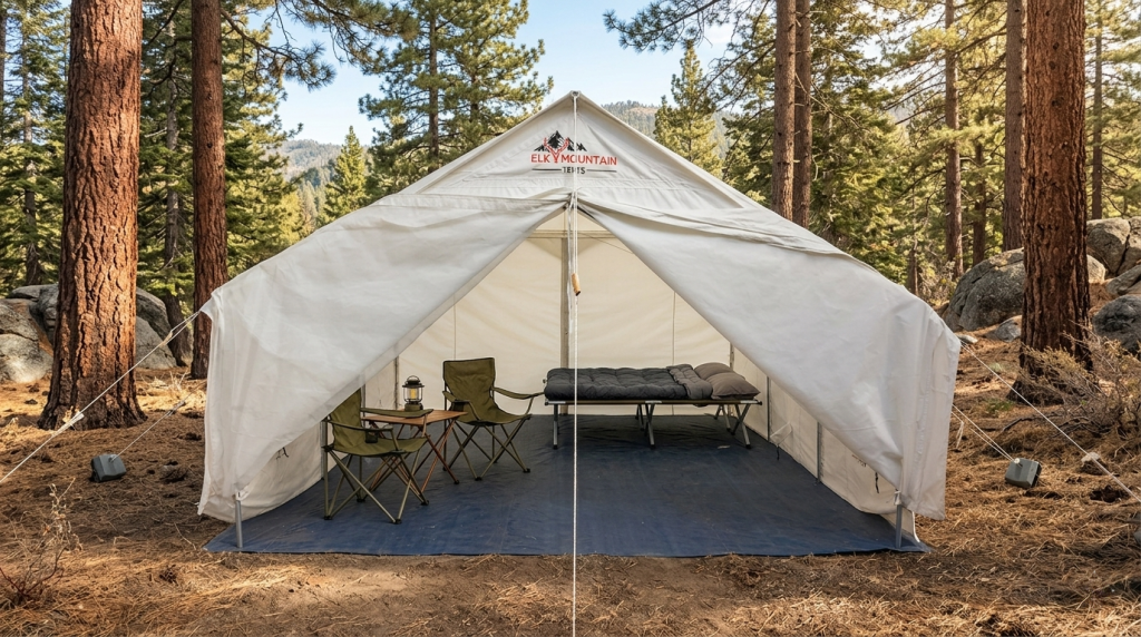 Elk Mountain Tents canvas wall tent pitched among pines, open front revealing camp chairs and a made-up cot
