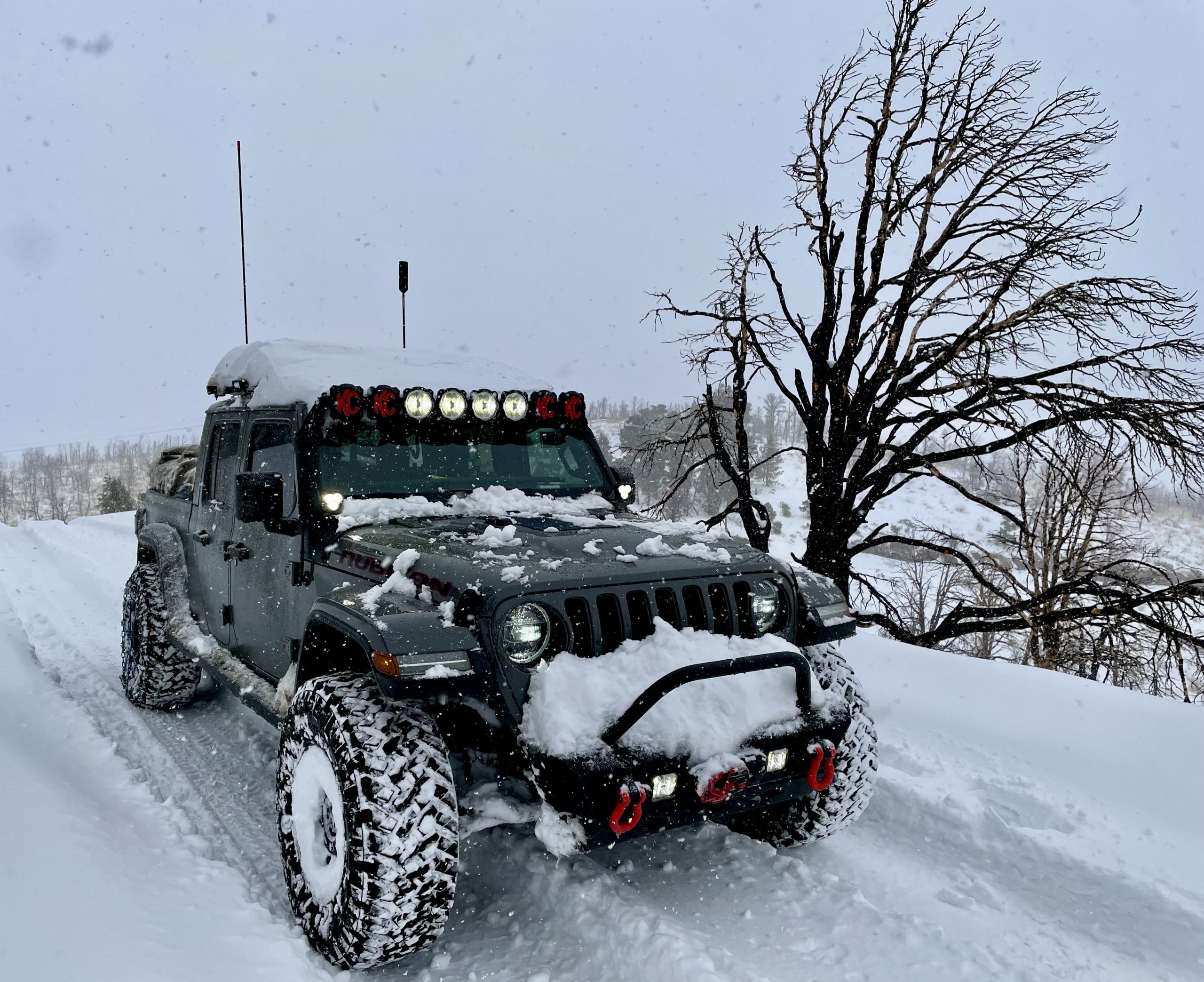 Snow-covered Jeep Gladiator Rubicon with light bar driving on a snowy road through falling snow