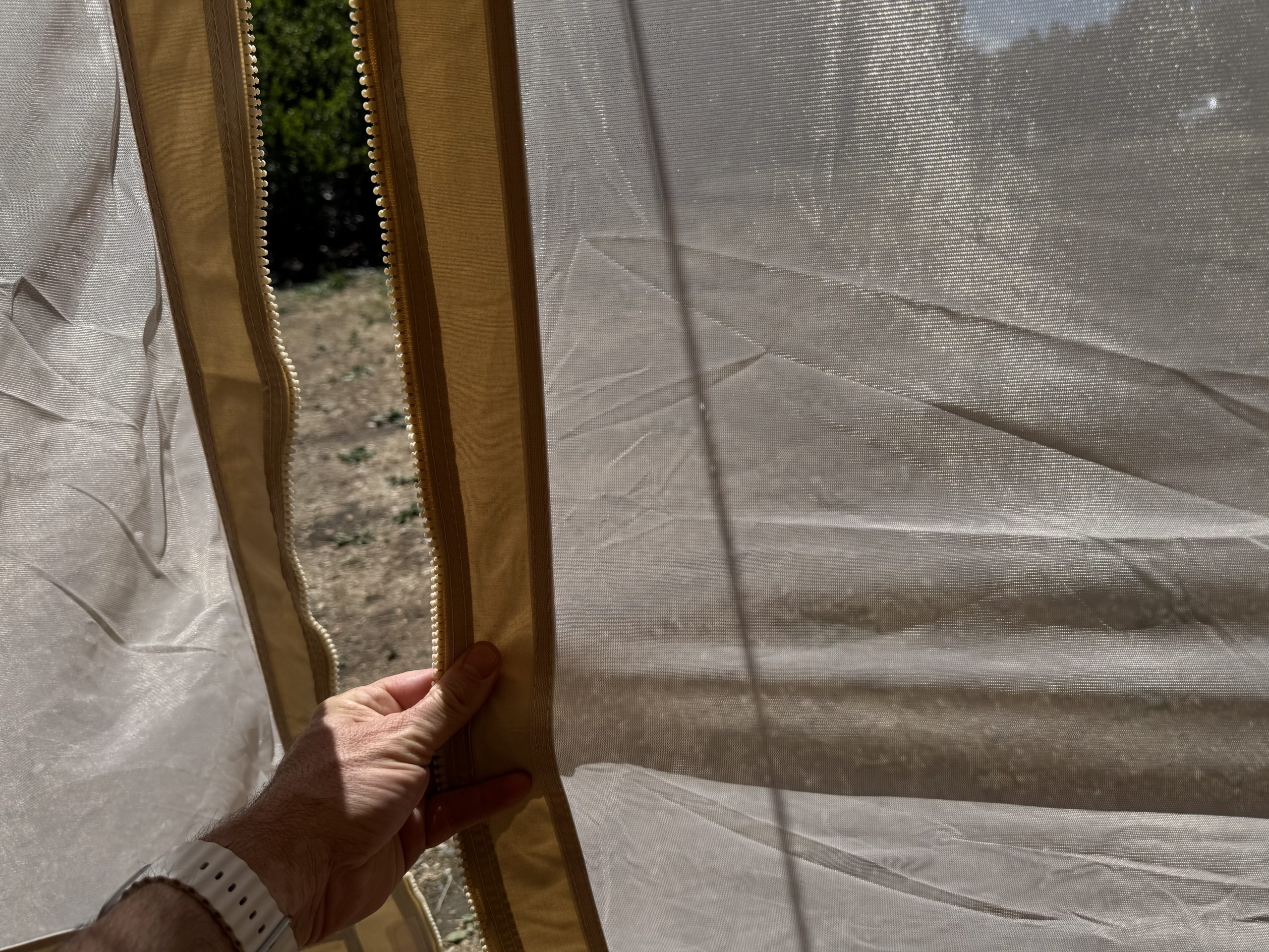 Close-up of the Stout 5M Pro bell tent's zipper, mesh screen, and stitching being inspected by hand.