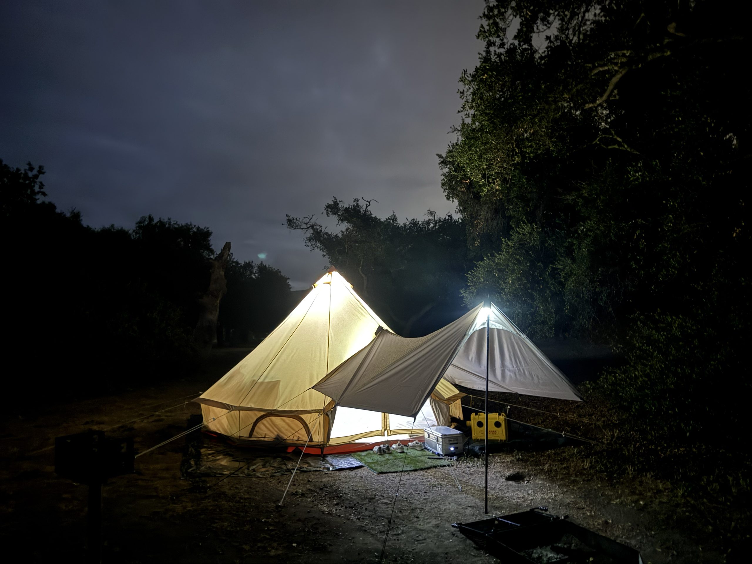 Stout 5M Pro bell tent lit up at night with a diesel heater running, tarp awning set up out front.
