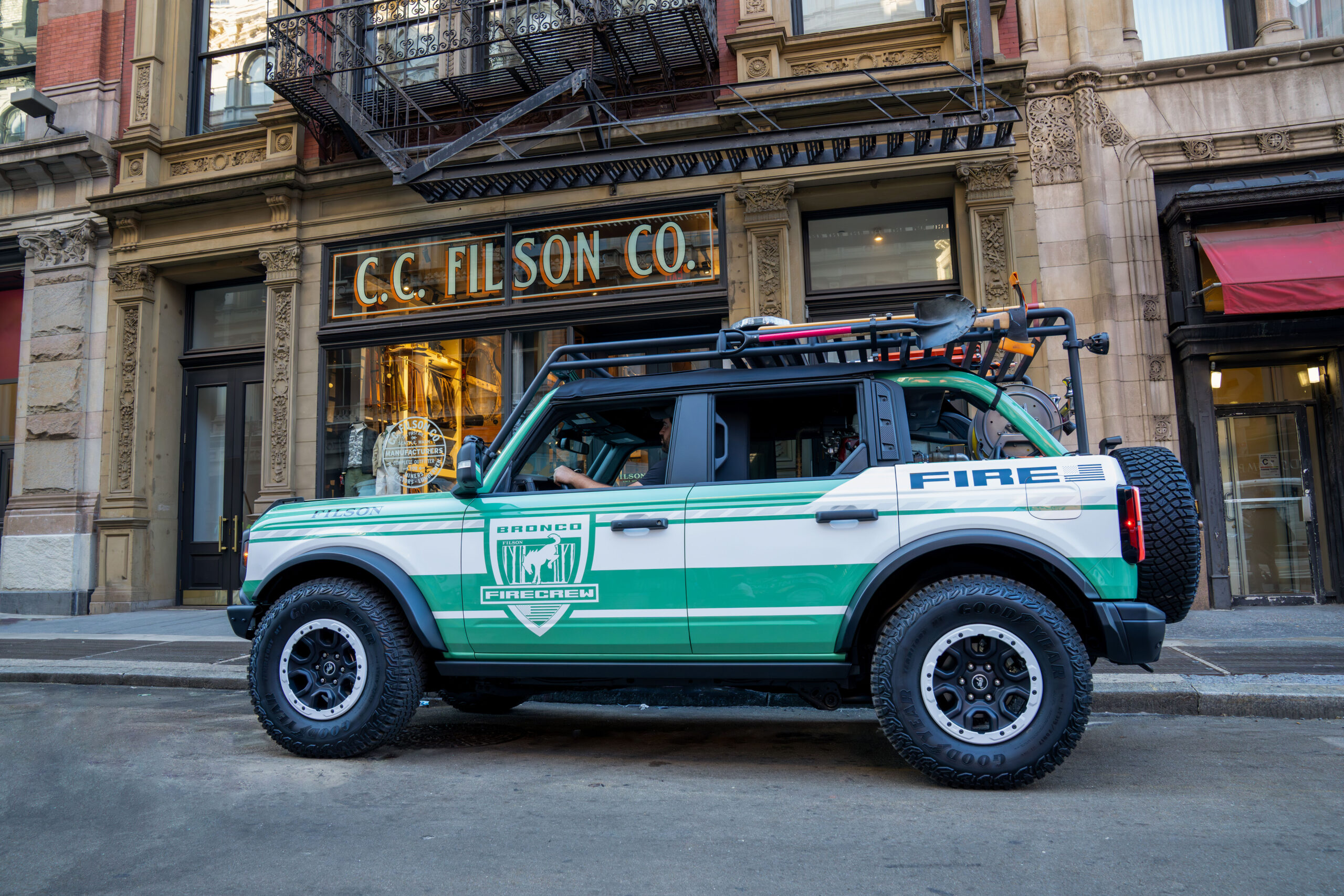 Green and white Bronco x Filson Firecrew edition with roof rack and spare tire parked outside the Filson storefront — manufacturer image
