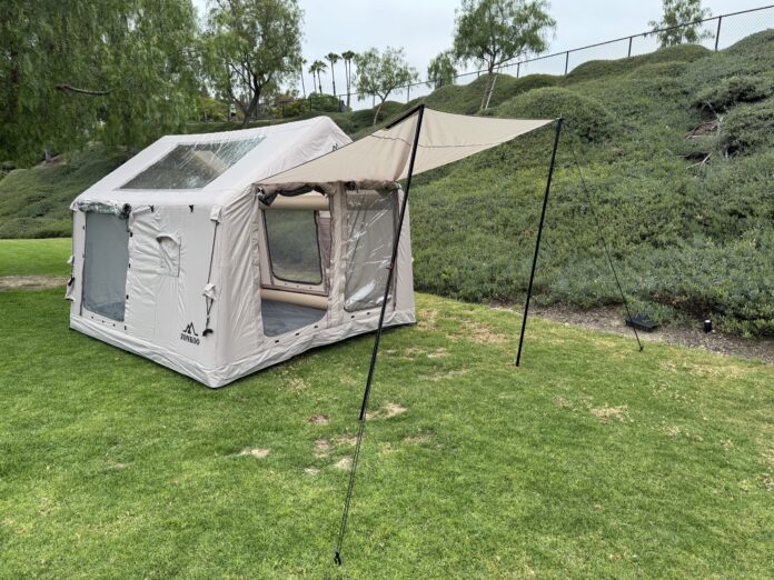 Tan Zonkoo Orion inflatable hot tent set up on grass with its front awning extended on poles