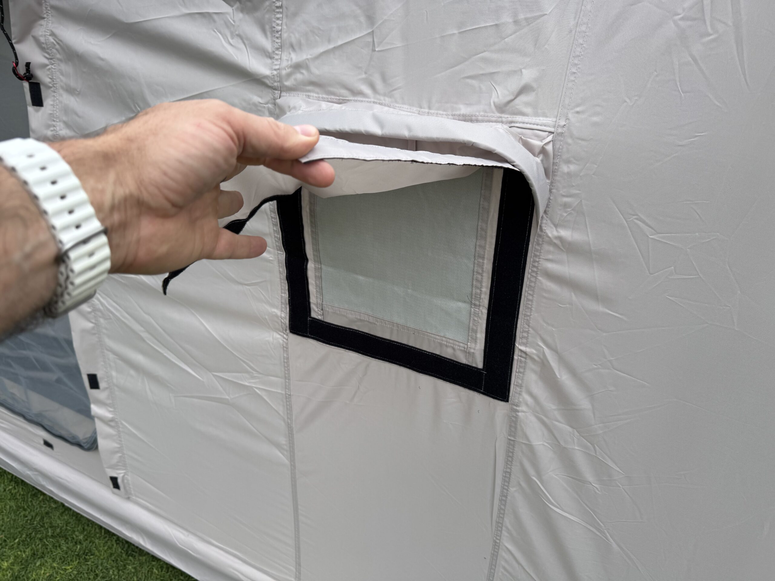 Hand opening a zippered mesh window flap on the tan fabric wall of the Zonkoo Orion inflatable tent