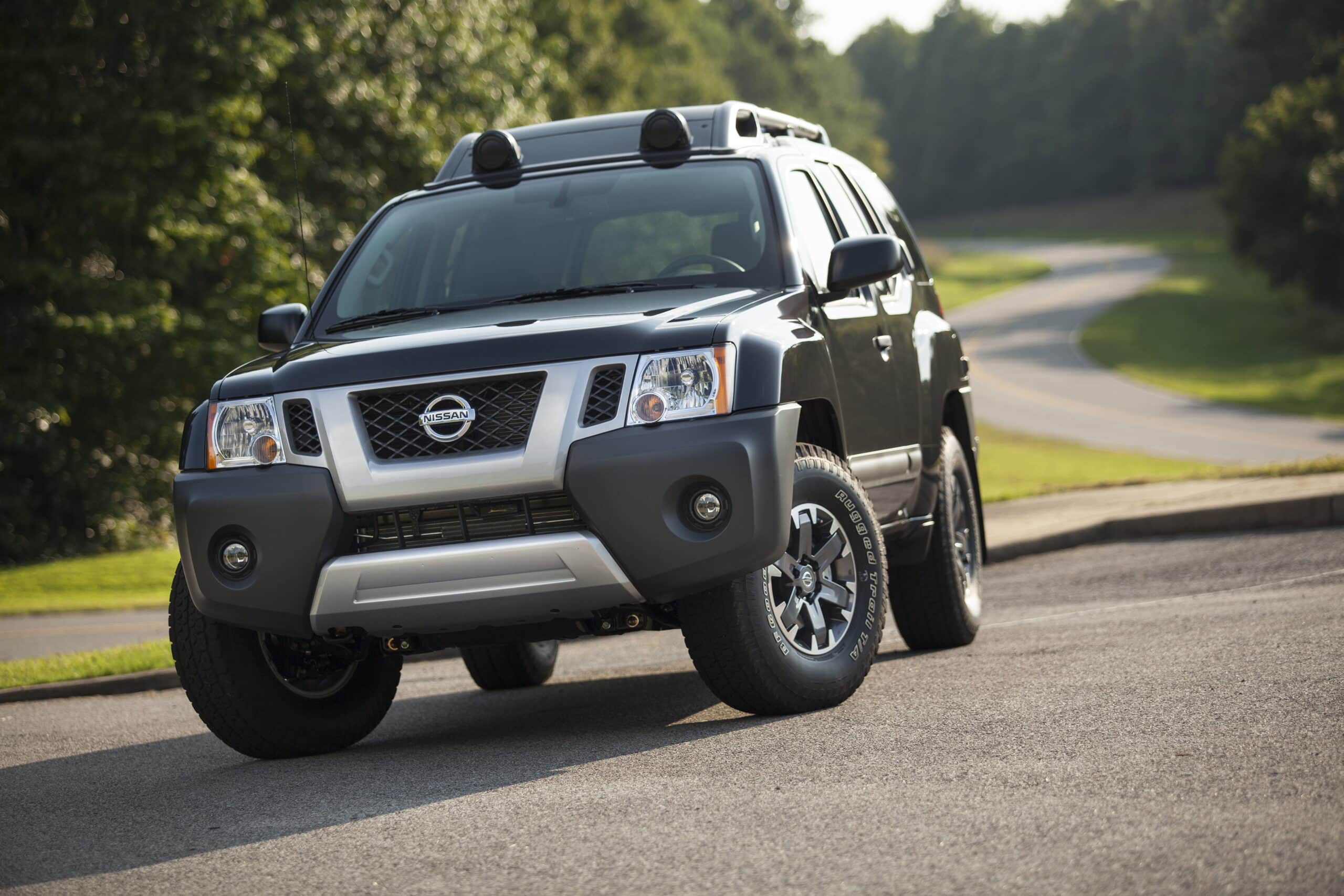 Black 2014 Nissan Xterra Pro-4X SUV with a roof rack parked on a paved road beside roadside trees