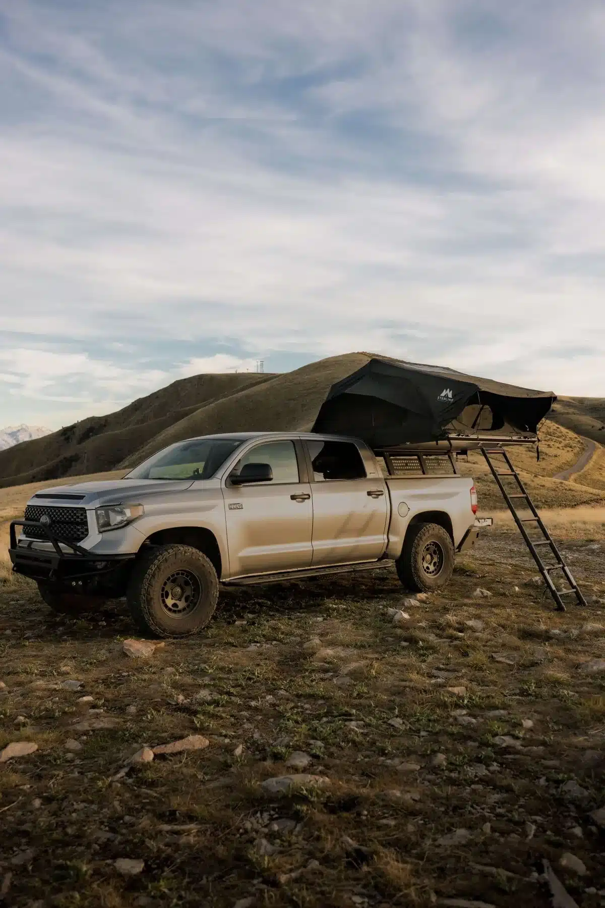 Black Basin aluminum hardshell rooftop tent mounted on a silver Toyota Tundra parked on a grassy hilltop
