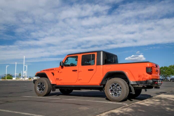 Orange Jeep Gladiator Rubicon crew cab pickup parked in an empty lot under a partly cloudy sky