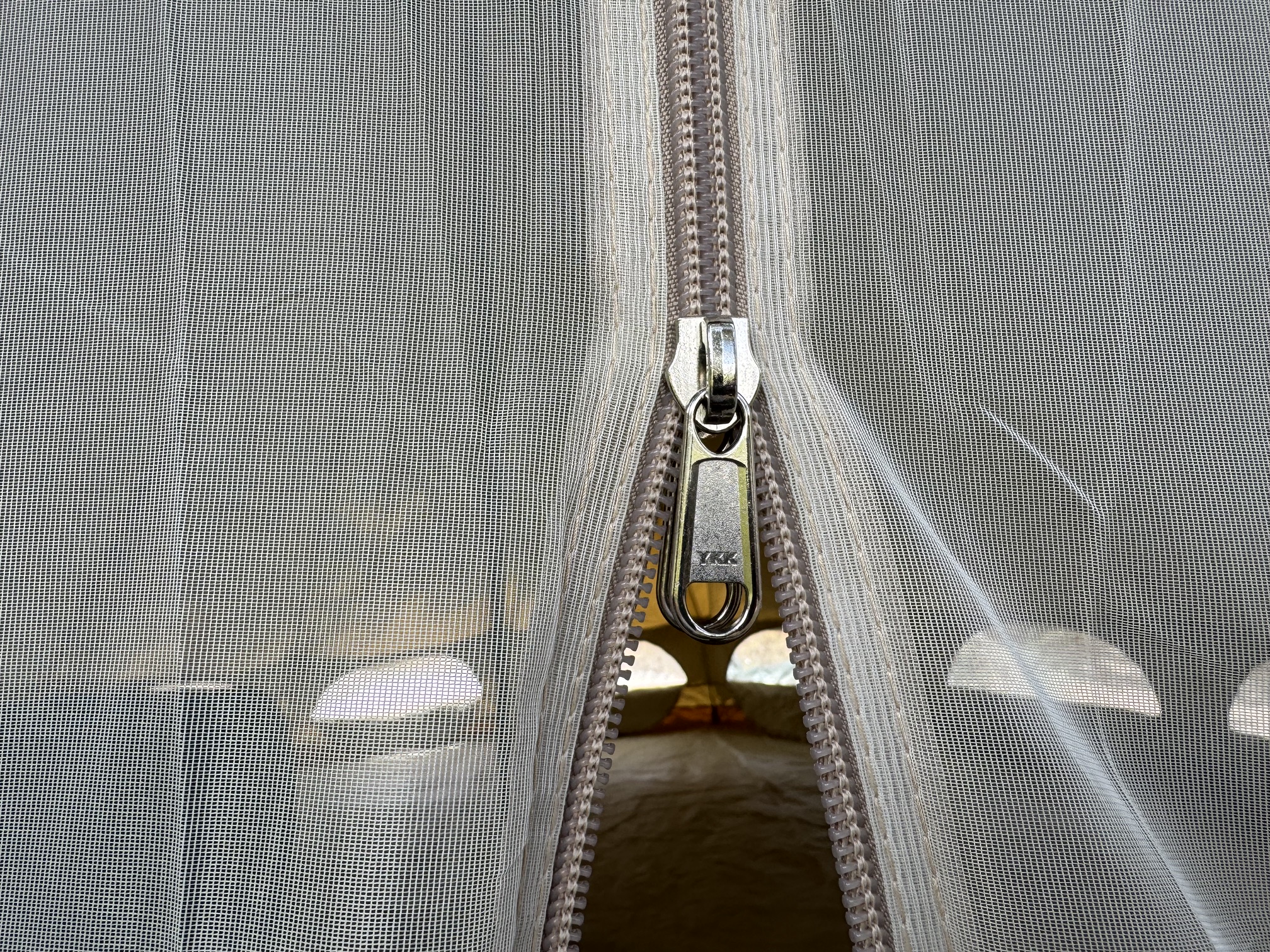 Close-up of a mesh tent door zipper partly open, revealing the bell tent interior and bedding beyond