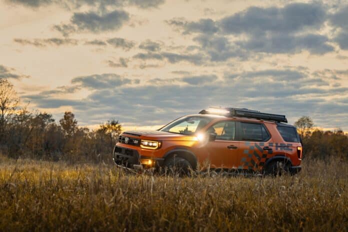 Orange 2027 Honda Passport TrailSport with roof light bar parked in tall golden grass at sunset