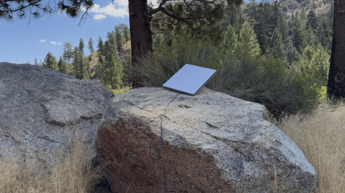 Gray Starlink Mini dish on a granite boulder among pines, the current model ahead of the Starlink Mini 2