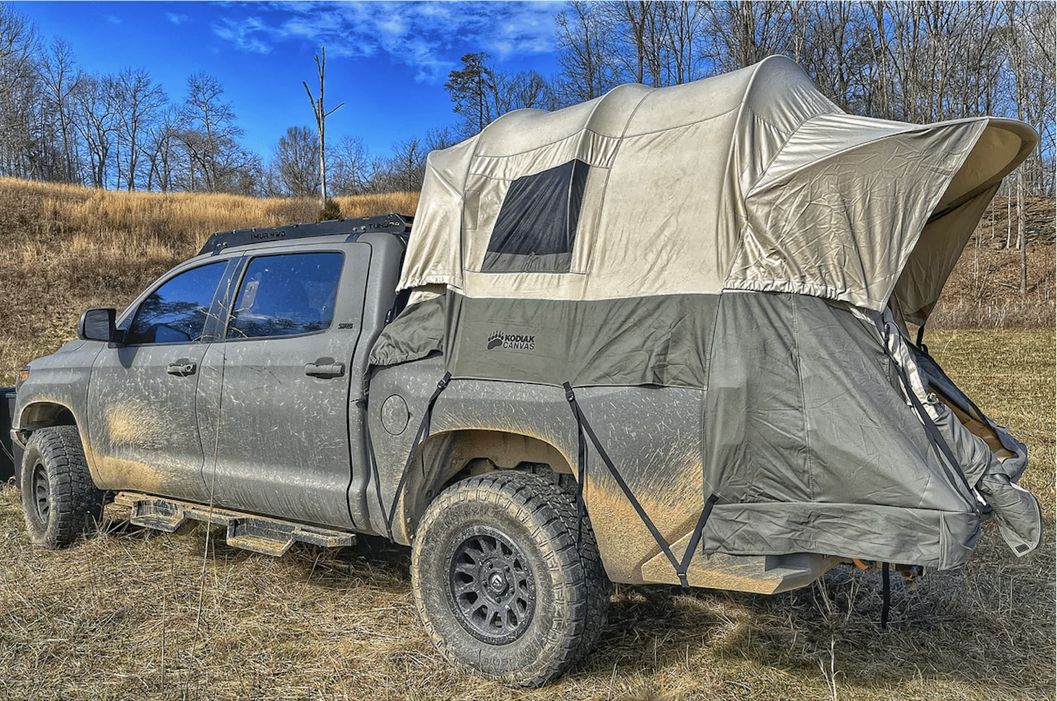 Kodiak Canvas truck bed tent on a gray Toyota Tundra parked in a dry grass field with bare trees behind it
