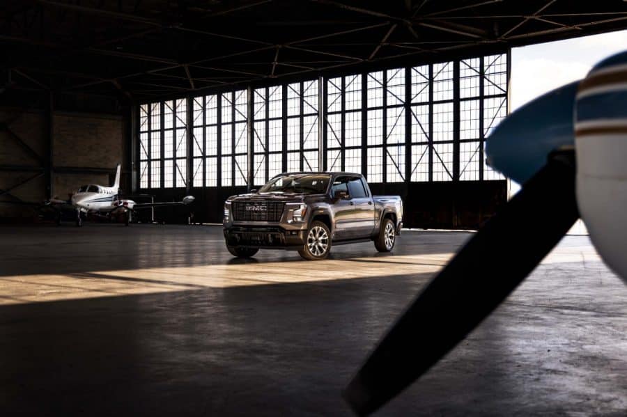 Gray GMC Sierra Denali Ultimate parked inside an airplane hangar beside small aircraft — manufacturer image