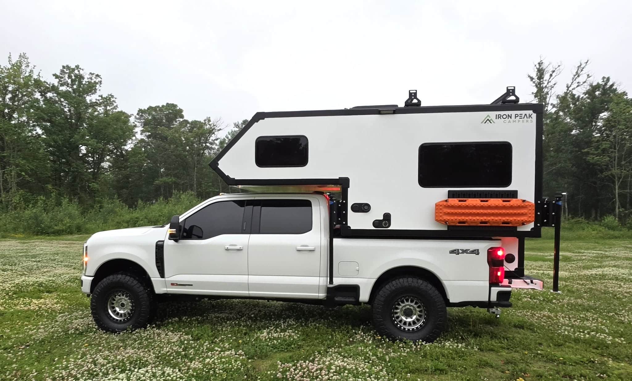 White Iron Peak Apex truck camper mounted on a white Ford Super Duty, shown in profile in a grassy field