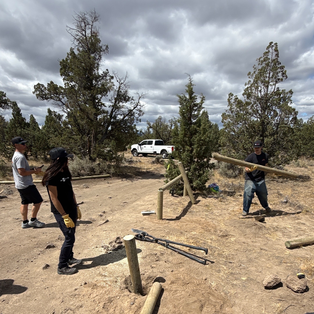 Volunteers and a white Toyota Super Duty truck at a trail worksite building wooden fence barriers under cloudy skies