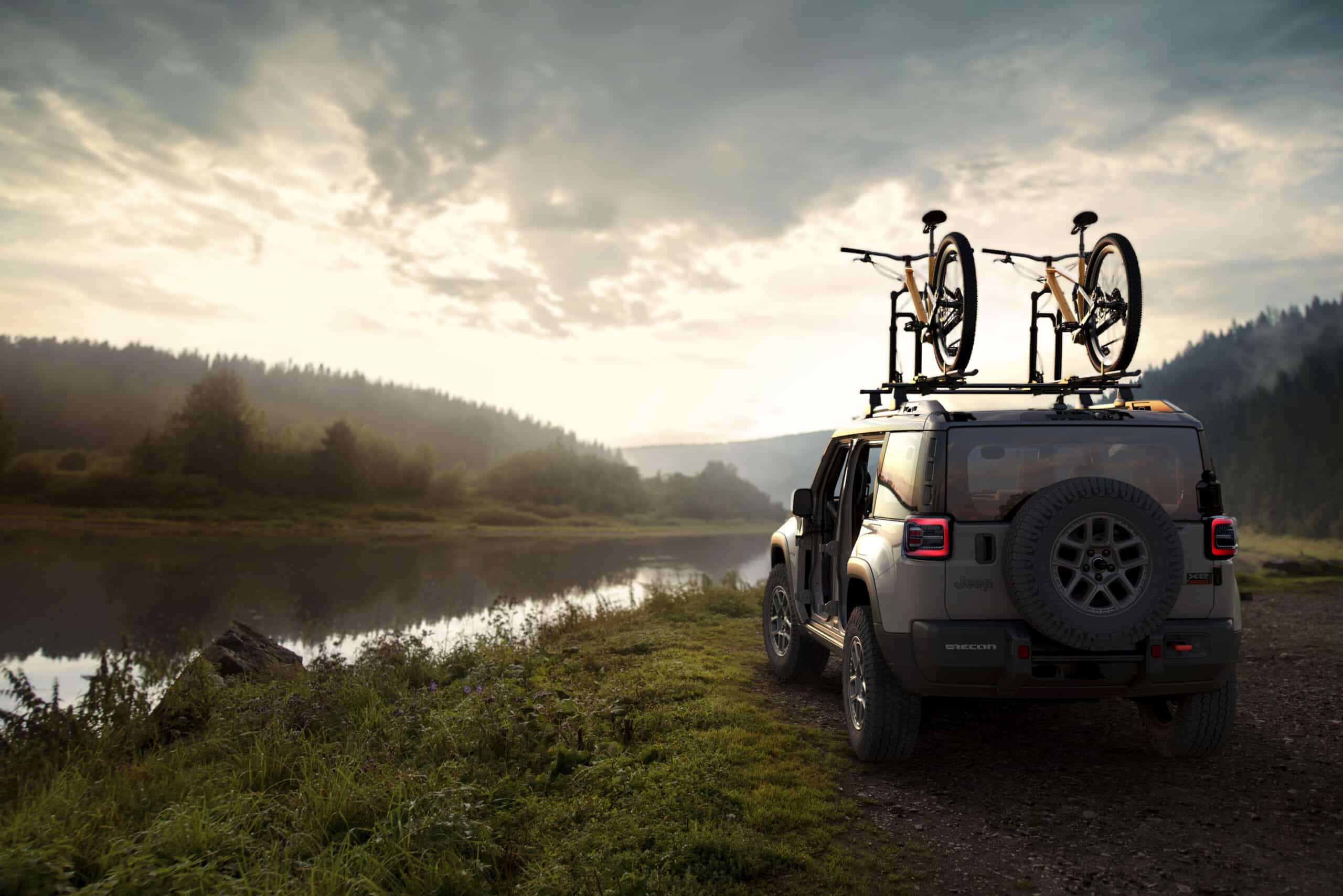 Tan 2026 Jeep Recon parked by a river at sunset with roof bikes and doors removed