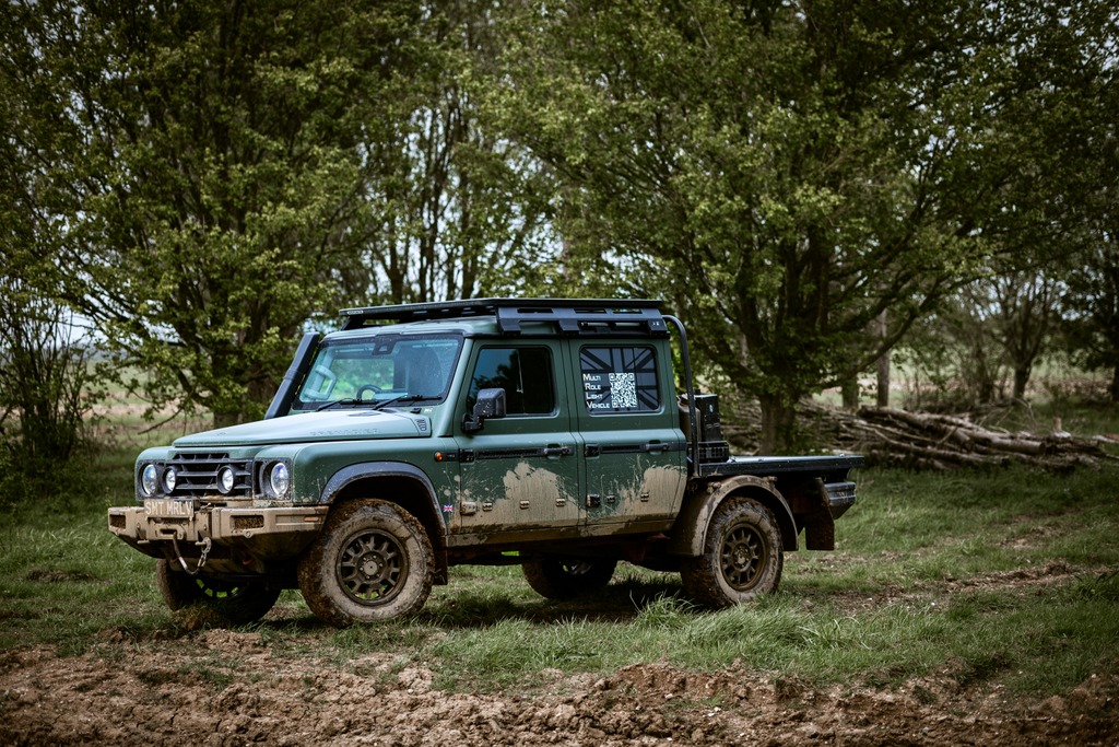 Ineos Grenadier MRLV in military green with a flatbed and roof rack parked on grass