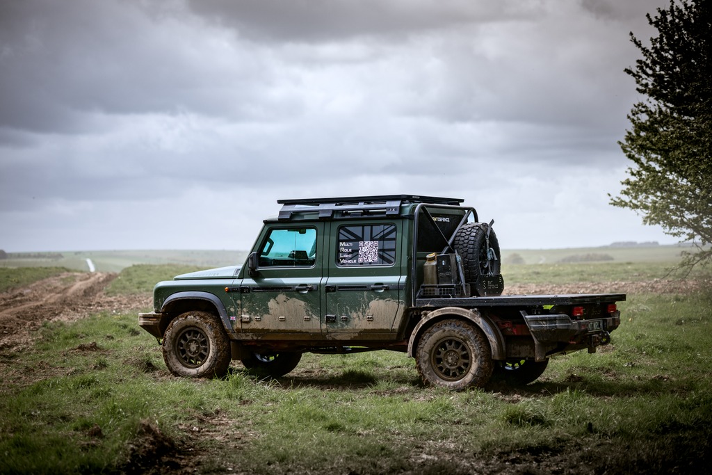 Military-spec Grenadier pickup parked in an open field under a heavy cloudy sky