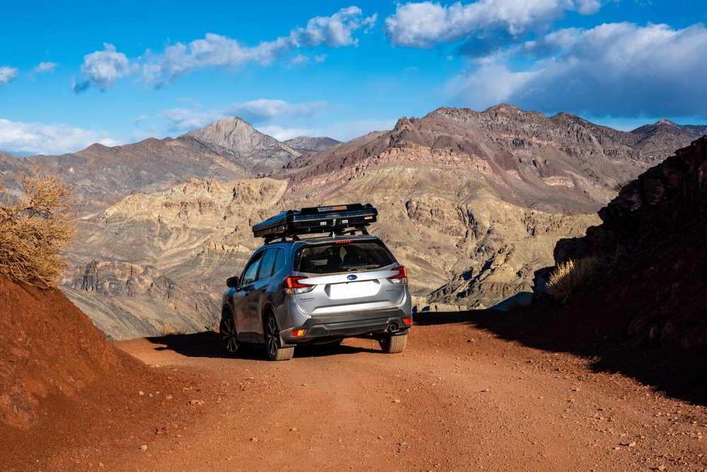 Silver Subaru Forester with a rooftop tent parked on a desert mountain trail above rugged badlands