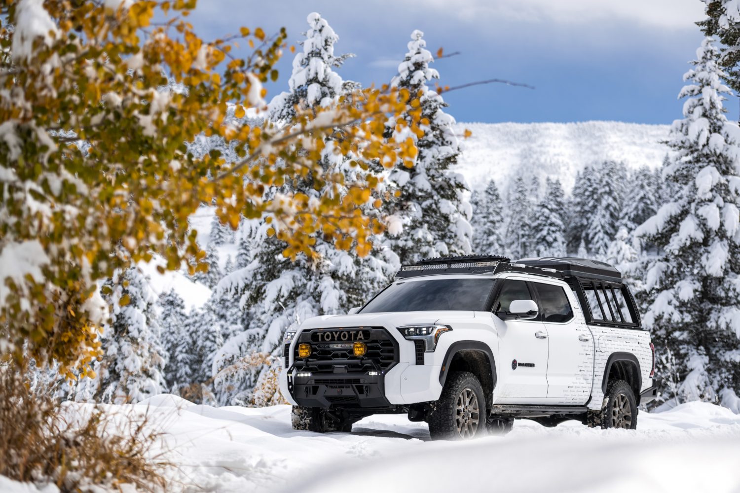 2027 Toyota Tundra Trailhunter driving through a snowy forest with autumn foliage in the foreground