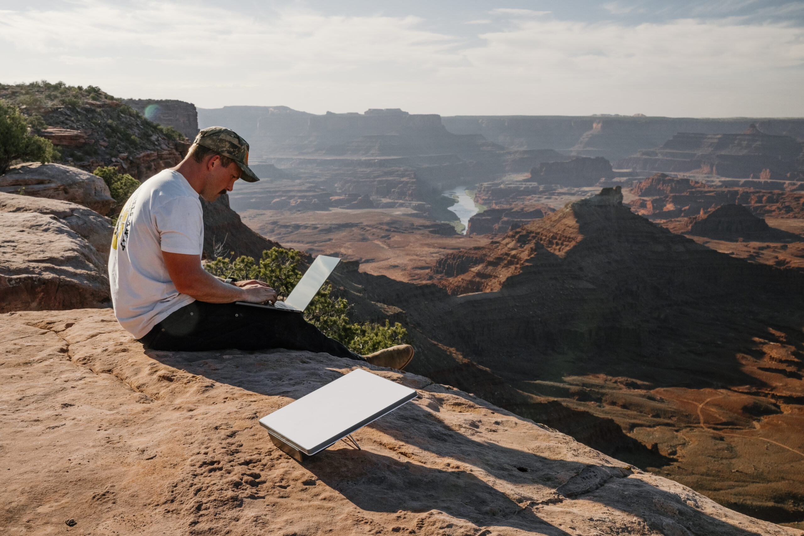Man working on a laptop next to a Starlink Mini dish with Devos AMPak 145 at a canyon-rim campsite near Moab, Utah