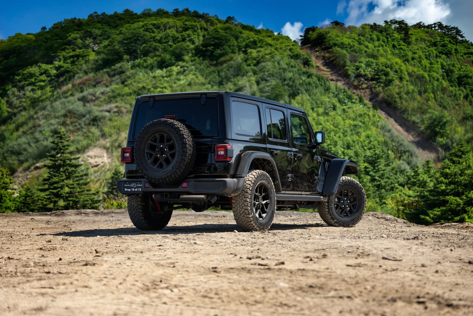 Rear three-quarter view of a black 2027 Jeep Wrangler Smoky Mountain showing the tailgate-mounted spare and the Drop 10 of 12 badge