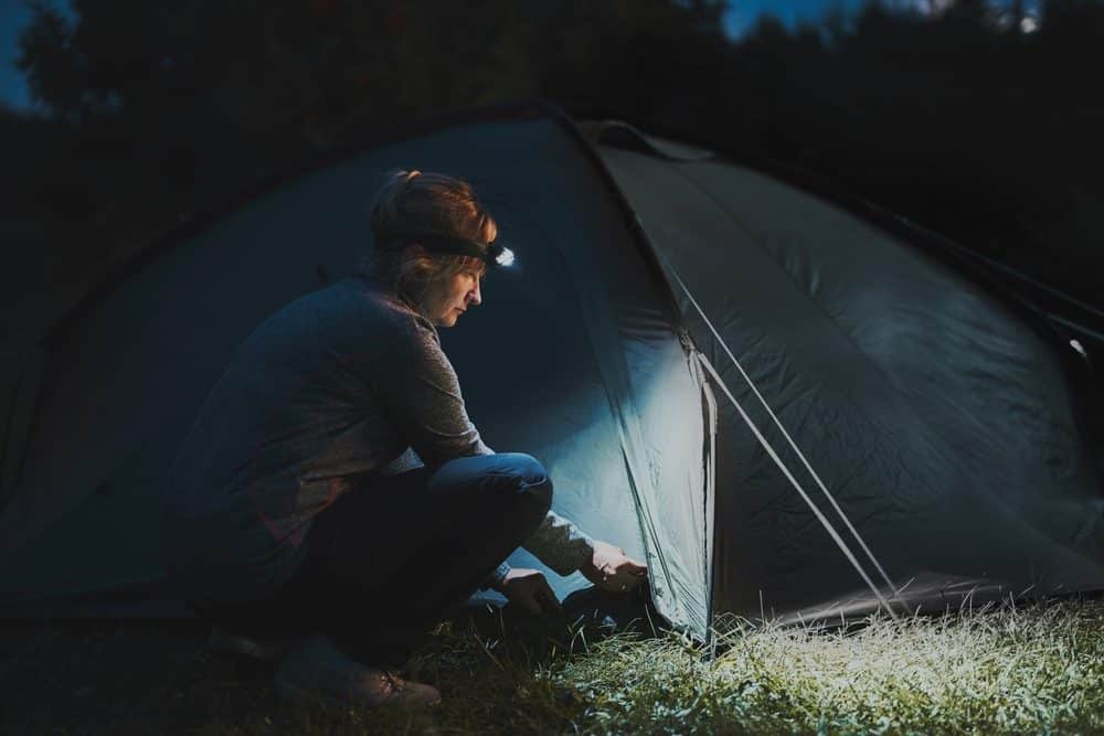 Camping tips for after dark, a camper wearing a headlamp while pitching a tent at dusk