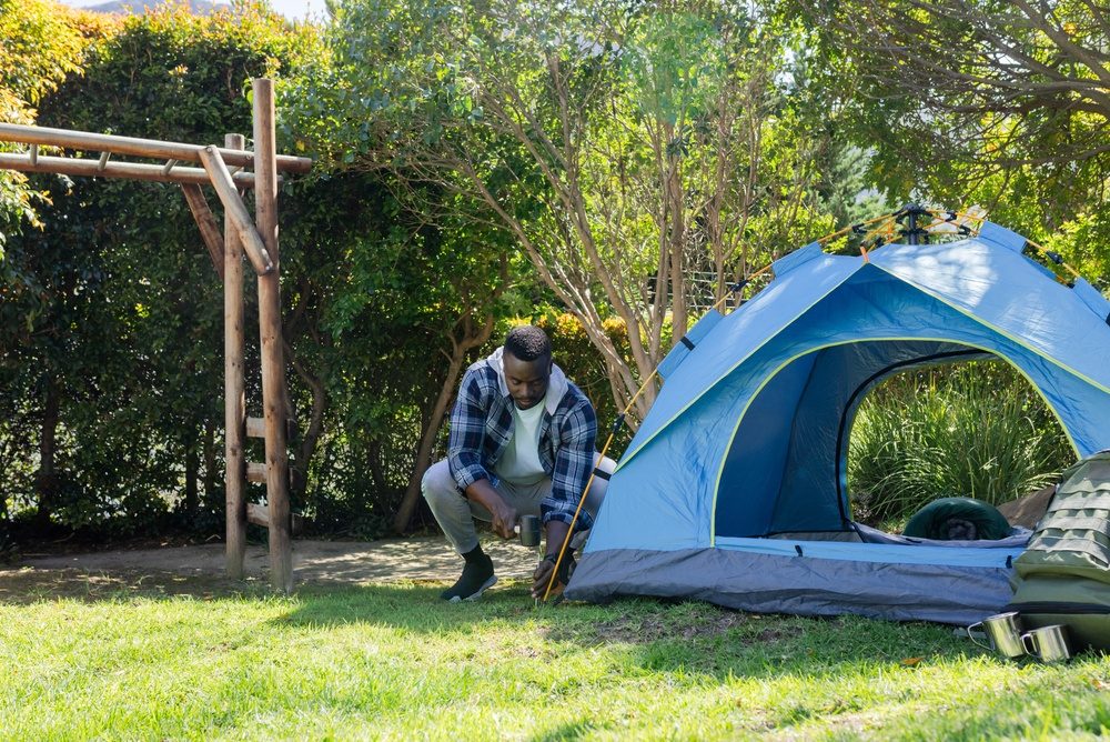 Man staking a blue dome tent on a backyard lawn
