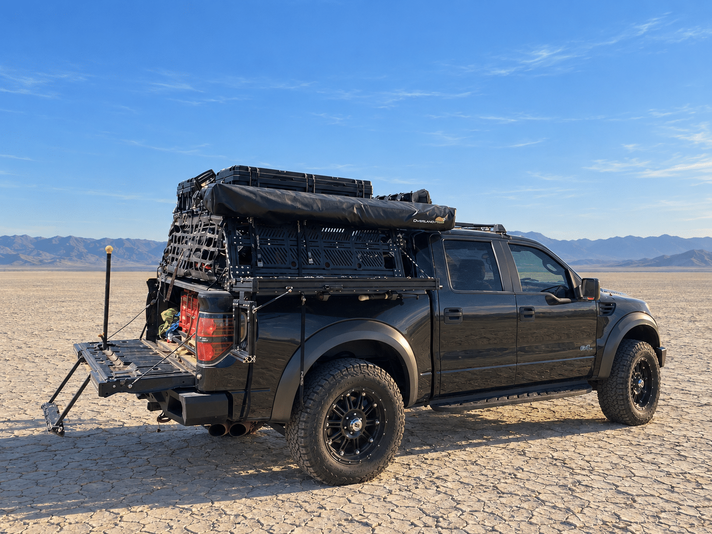 Truck bed step mounted to an existing bed rack, folded flush beneath two black cargo cases