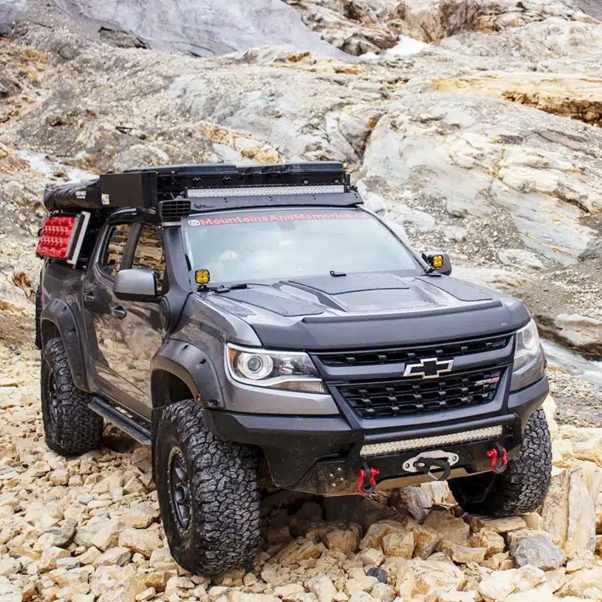 Gray Chevrolet Colorado ZR2 on rock with a rooftop tent, light bar and fuel cans filling the roof rack