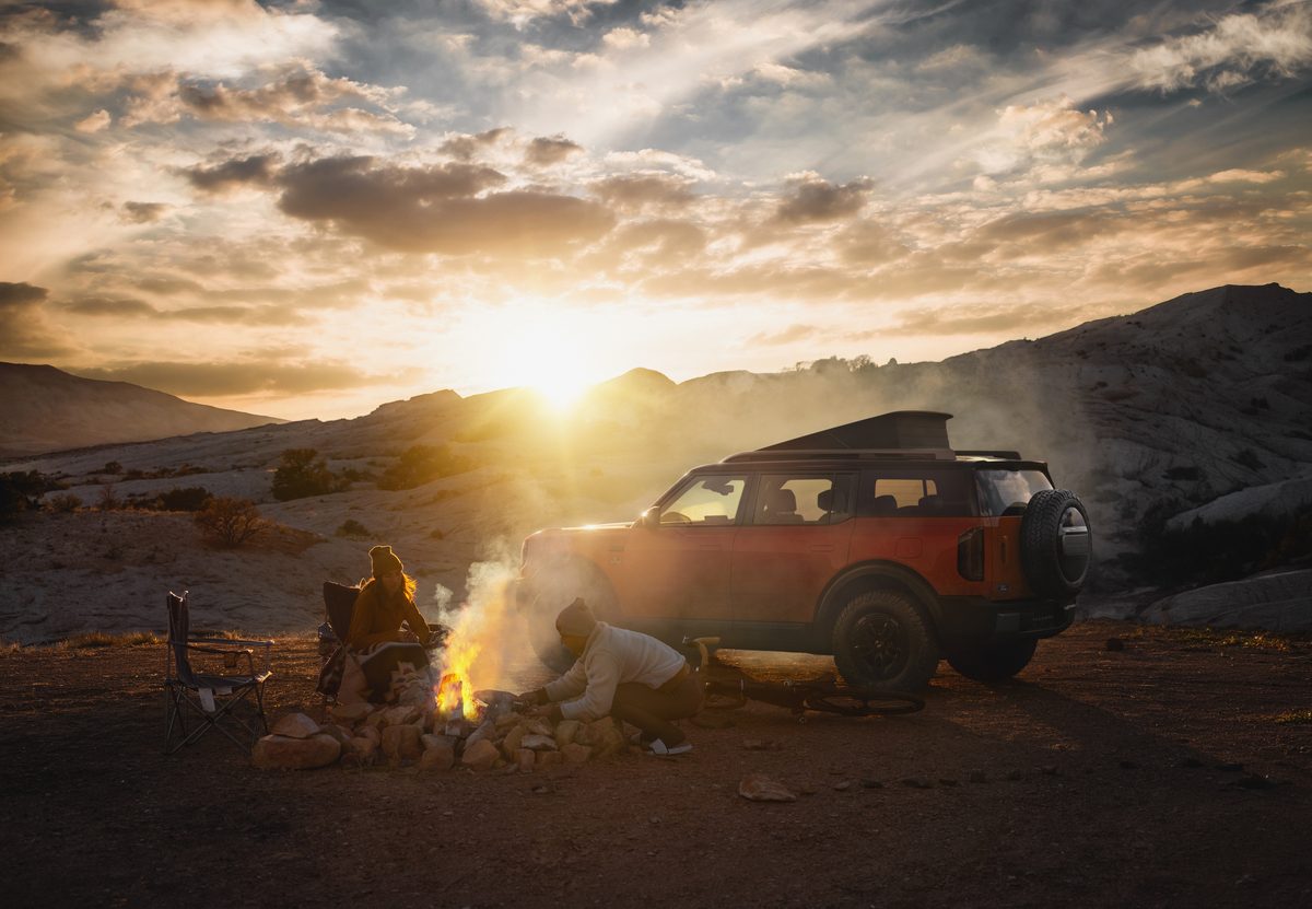 Orange Bronco Basecamp with the pop-up lift roof raised beside a campfire at sunrise