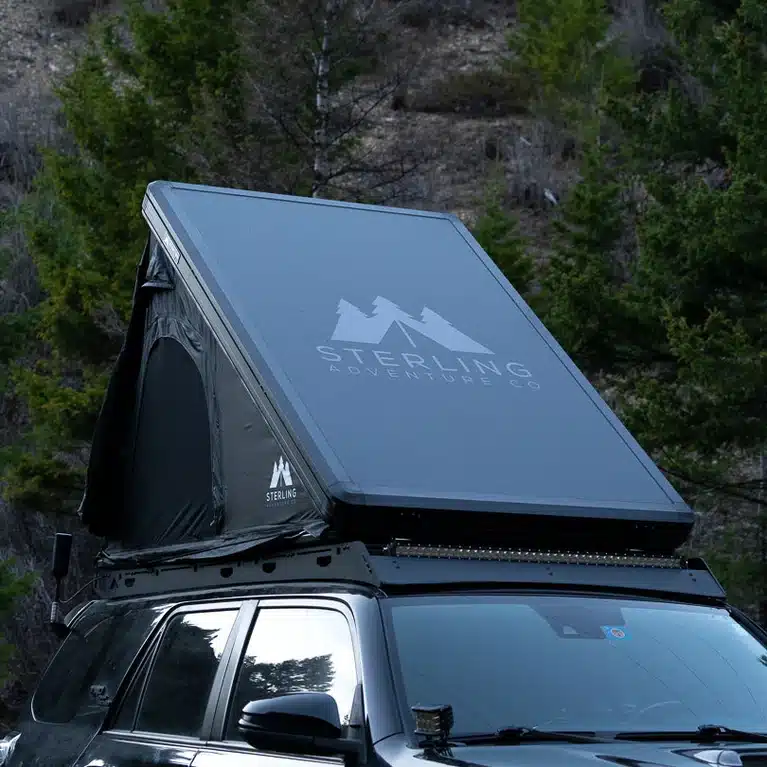 Wasatch Lite V2 rooftop tent with its aluminum lid raised on gas struts above a roof rack and front light bar