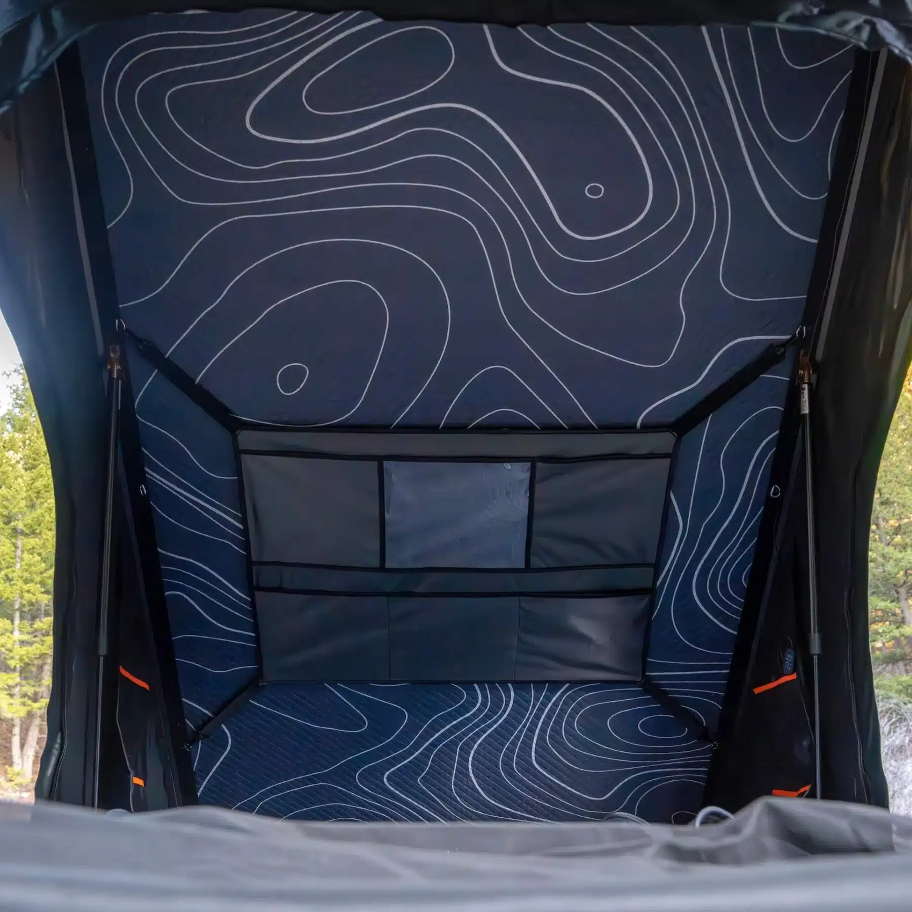 Inside the Wasatch Lite V2 rooftop tent showing the topographic-print mattress, six-pocket storage organizer, and gas struts