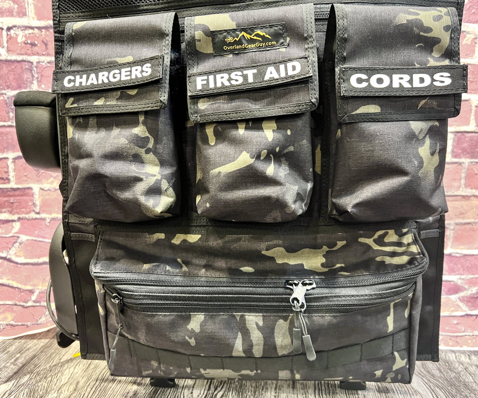 Camo seat organizer with pockets labeled chargers, first aid and cords, a pocket-by-pocket approach to Jeep Wrangler storage