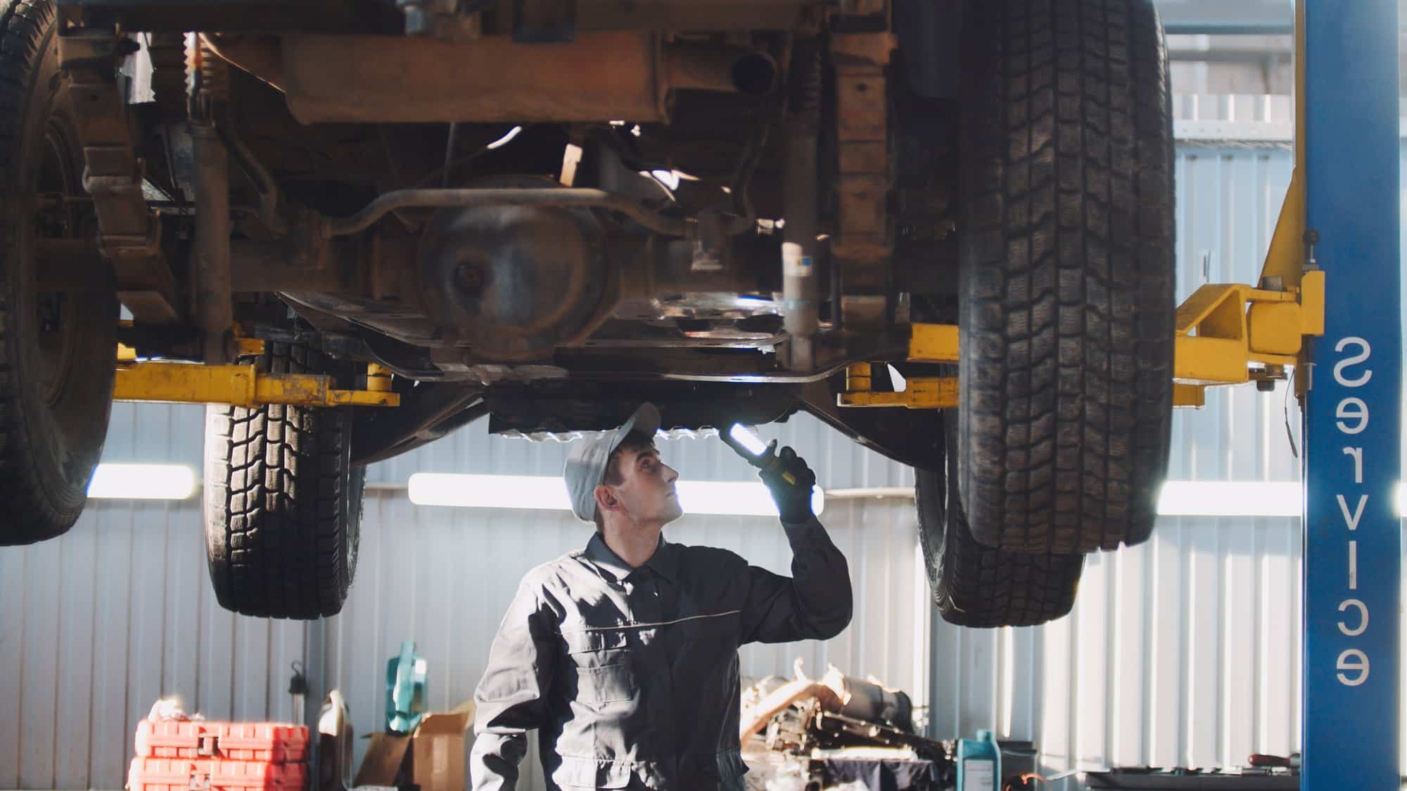Recall repair at a dealer Technician using a work light to inspect the underside of an SUV on a shop lift during a recall visit