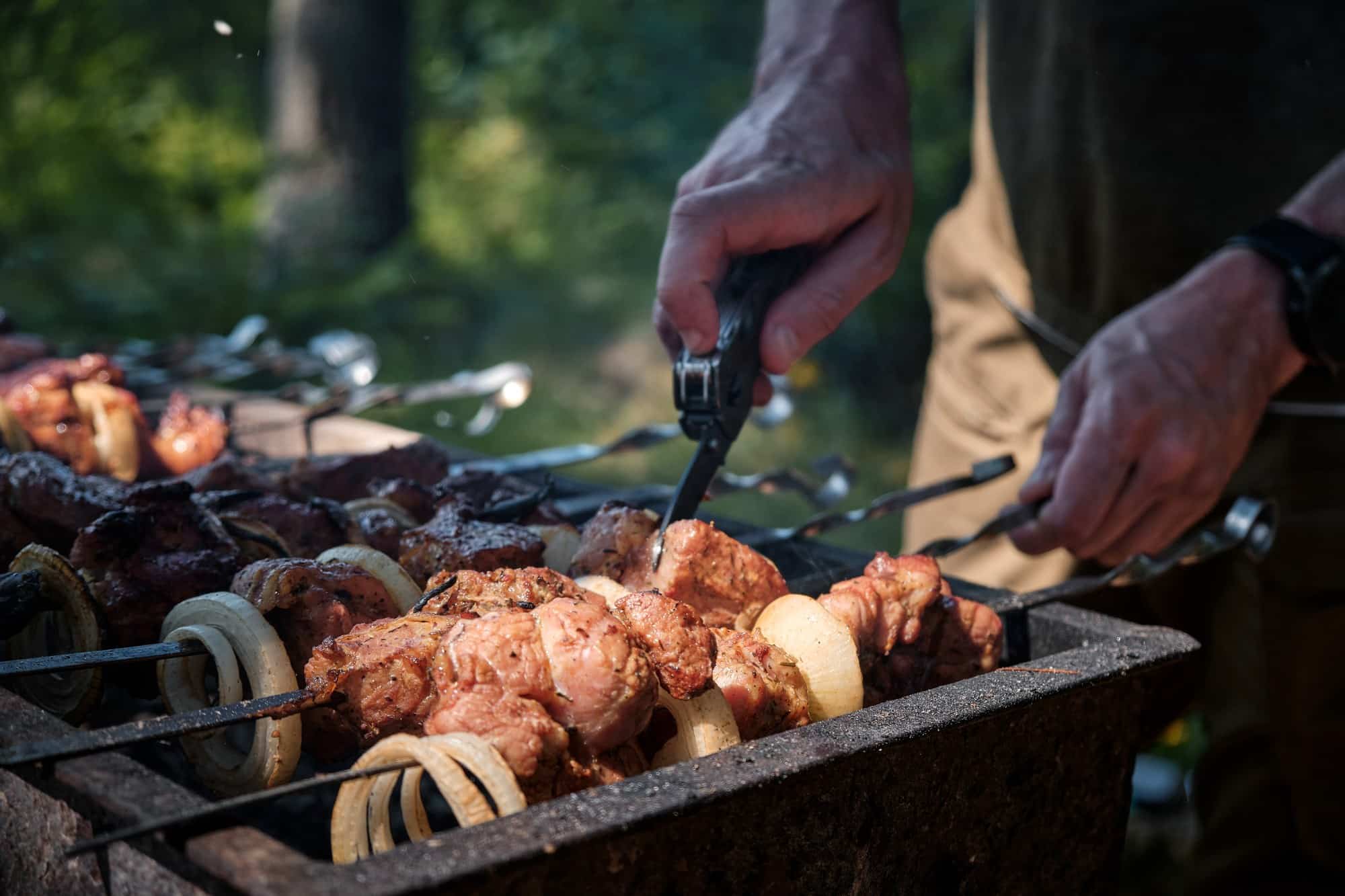 Camp food prep with a folder Folding pocket knife cutting grilled meat on a campfire grill at camp