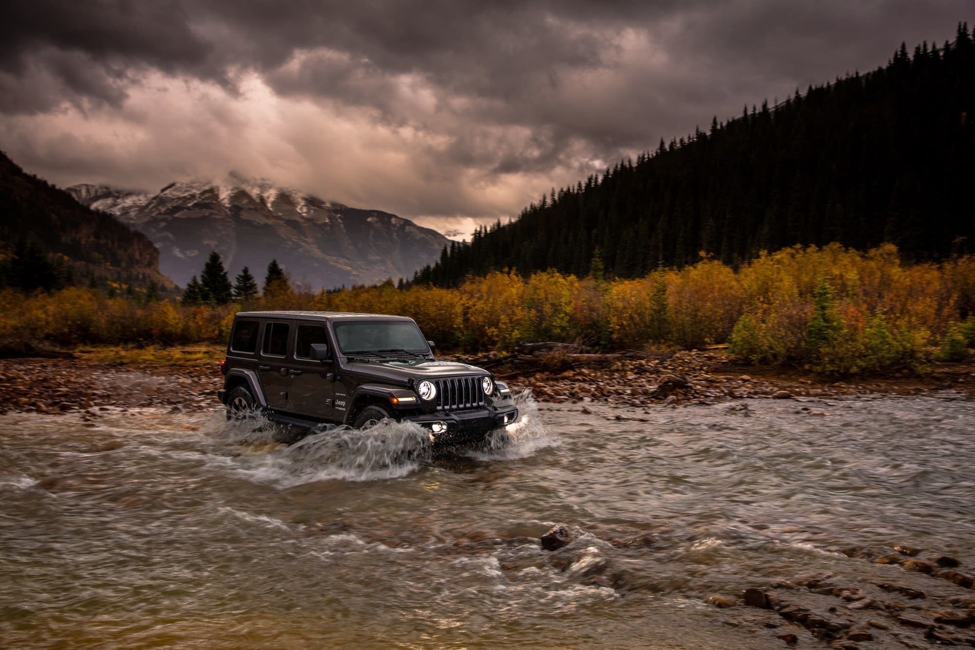 Black Jeep Wrangler Sahara JL fording a rocky mountain river with its front wheels in the water