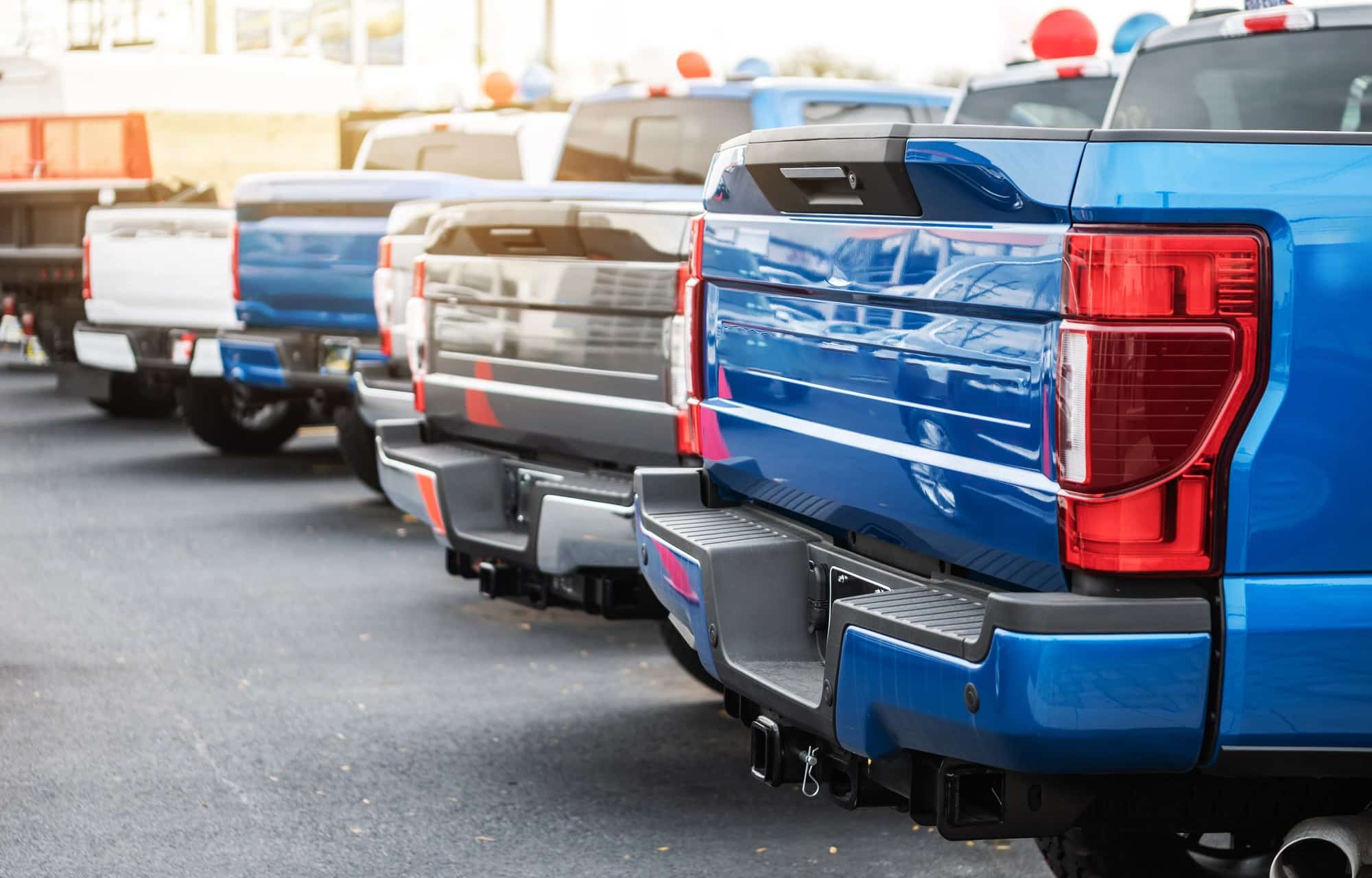 Row of new full-size pickups parked tailgate to tailgate on a dealer lot
