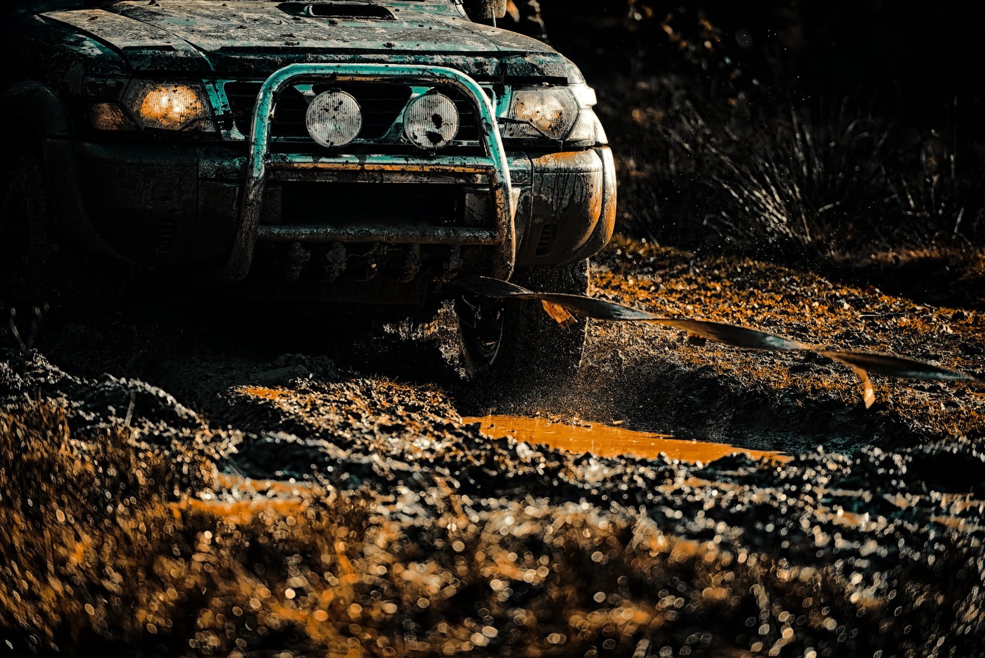 Off-road 4x4 with round auxiliary lights on a bull bar driving through mud at night