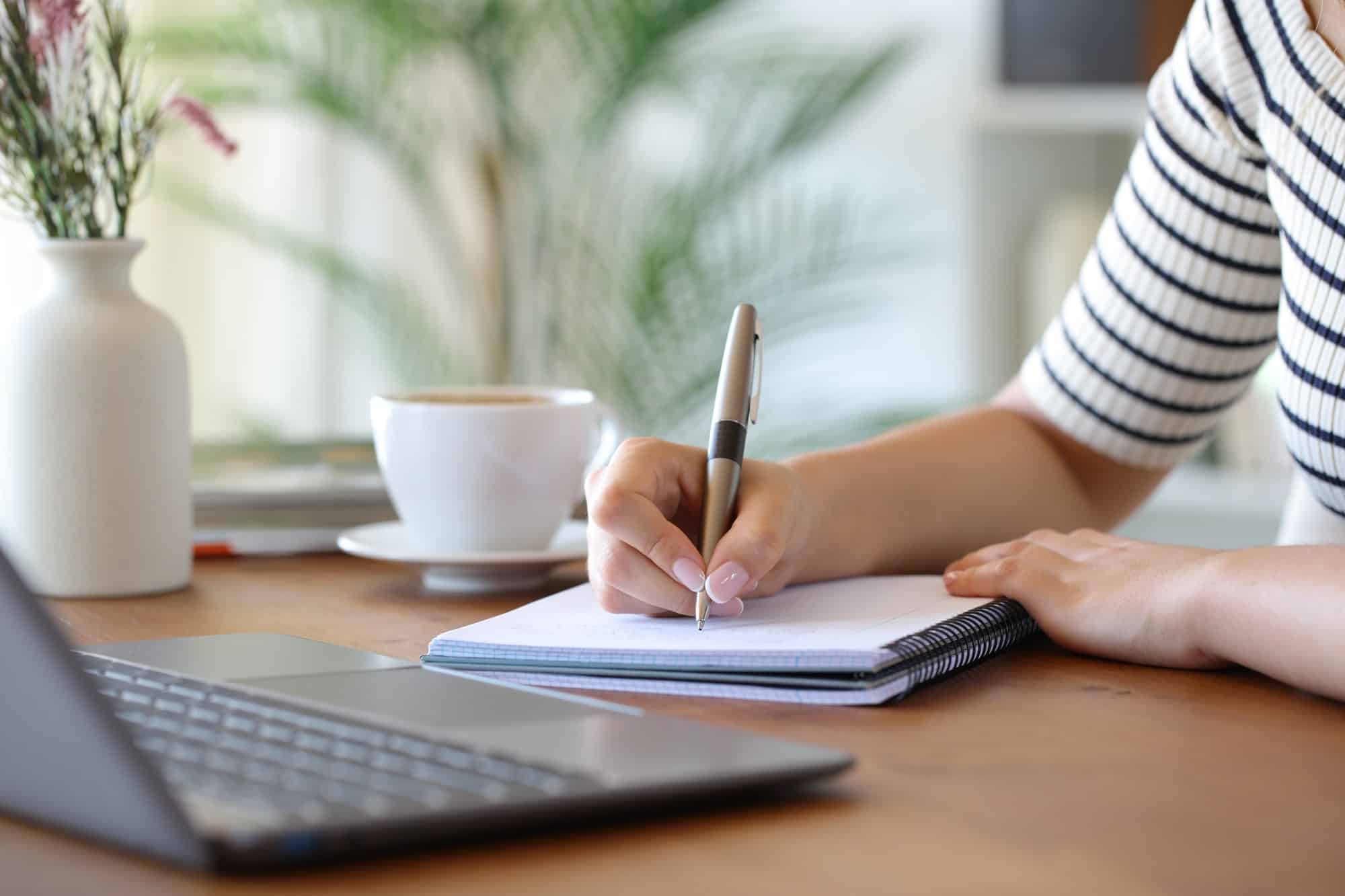Studying for the Technician exam Hand writing study notes in a notebook beside a laptop on a wooden desk