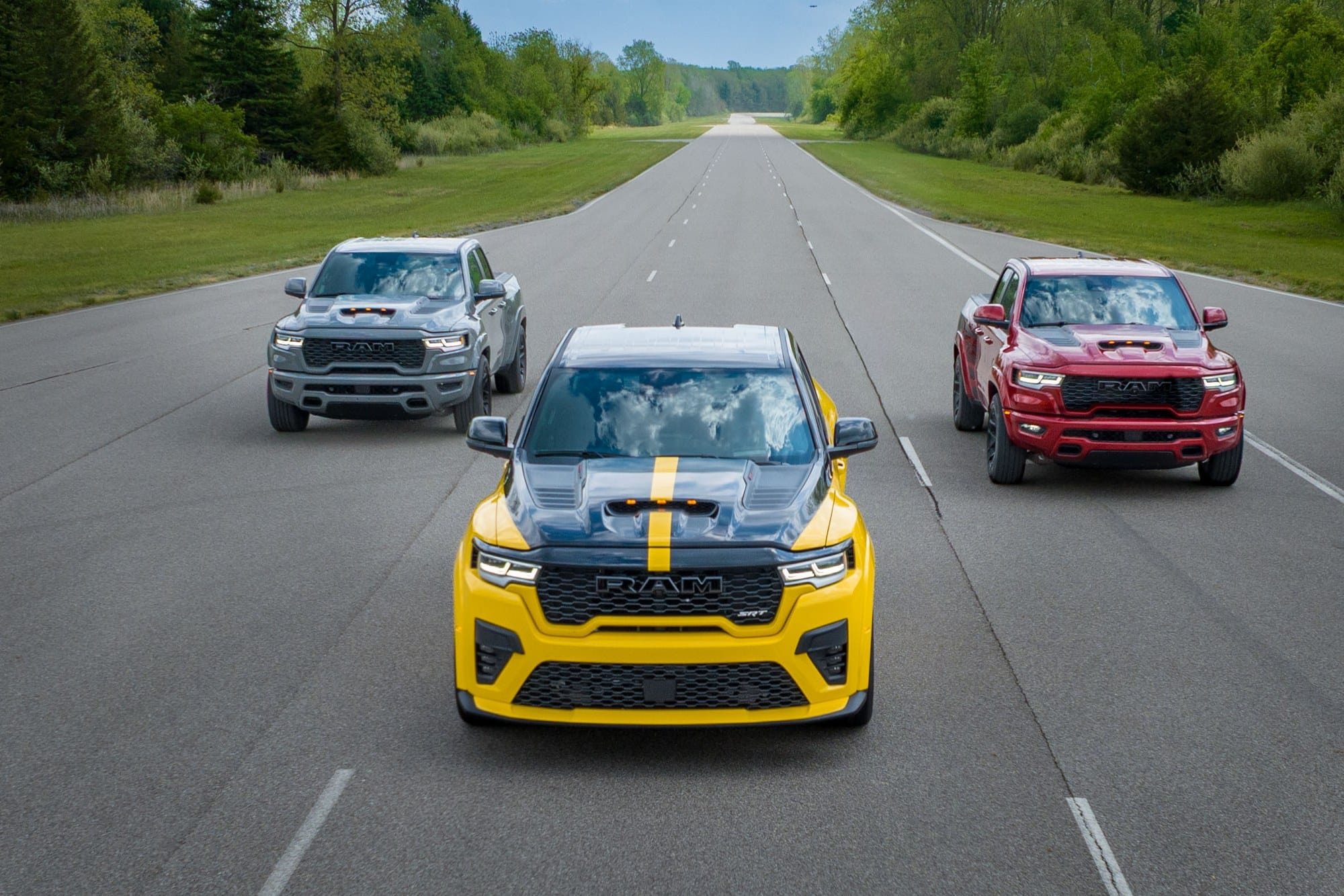 Ram 1500 Rumble Bee trio on a test road Gray, yellow, and red 2027 Ram 1500 Rumble Bee trucks driving on a paved test road