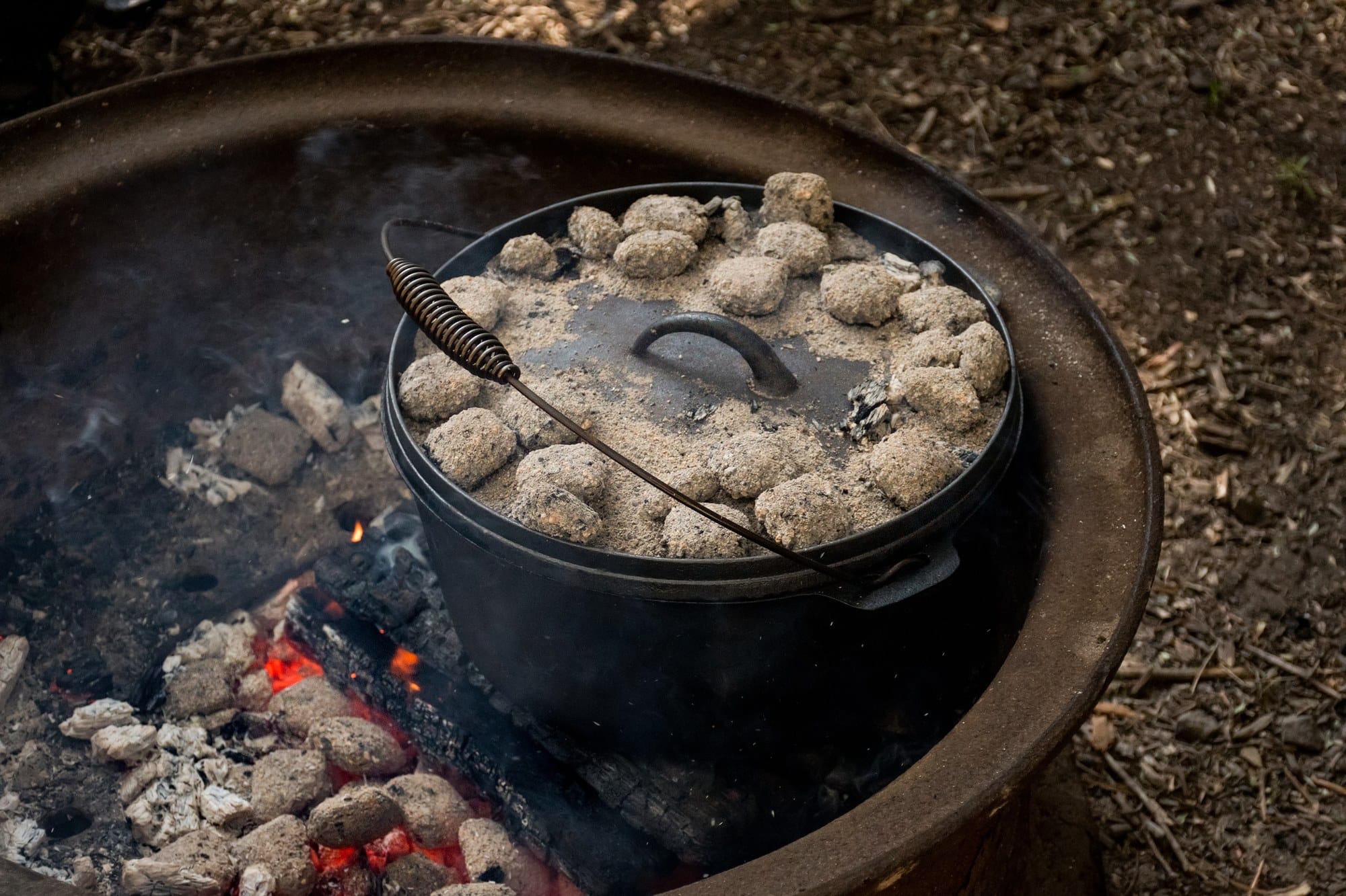 Dutch oven over campfire coals Cast iron Dutch oven with charcoal briquettes on the lid over campfire coals