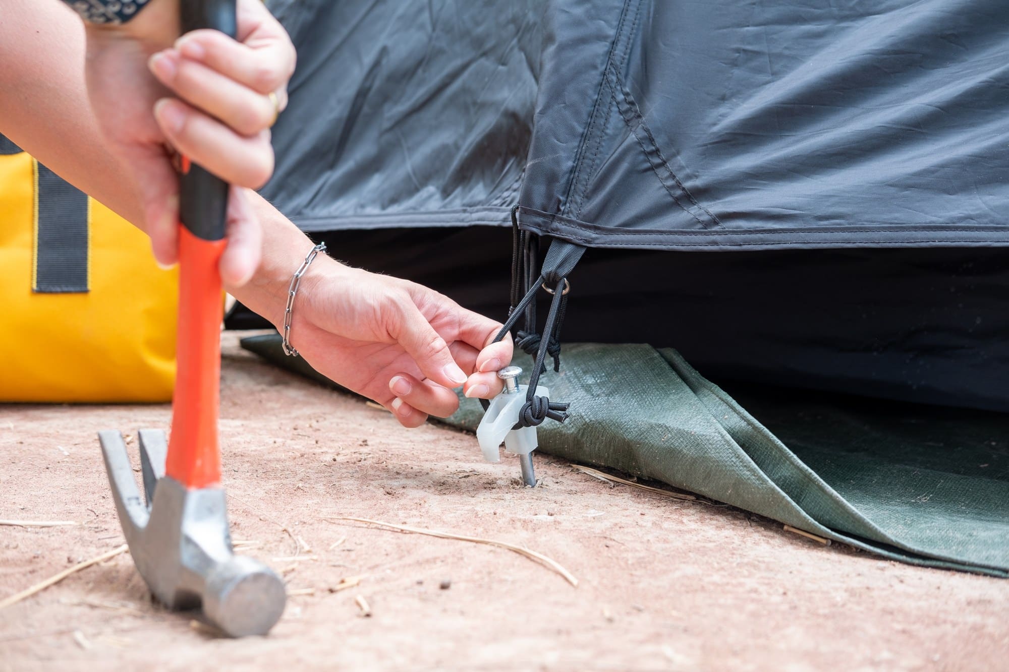 Staking a tent corner in hard ground Hammer driving a tent stake into hard ground at a tent corner