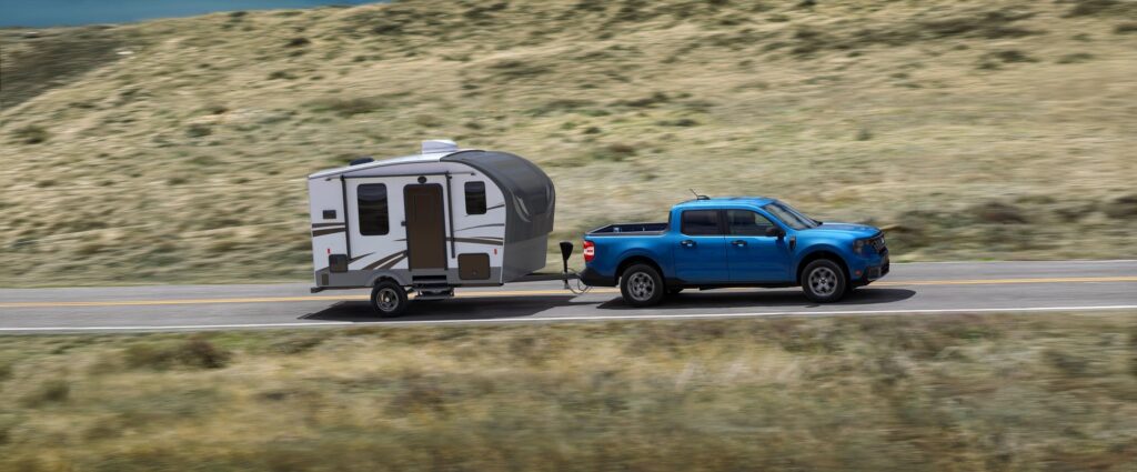 Ford Maverick XLT in blue towing a small camper trailer on a highway