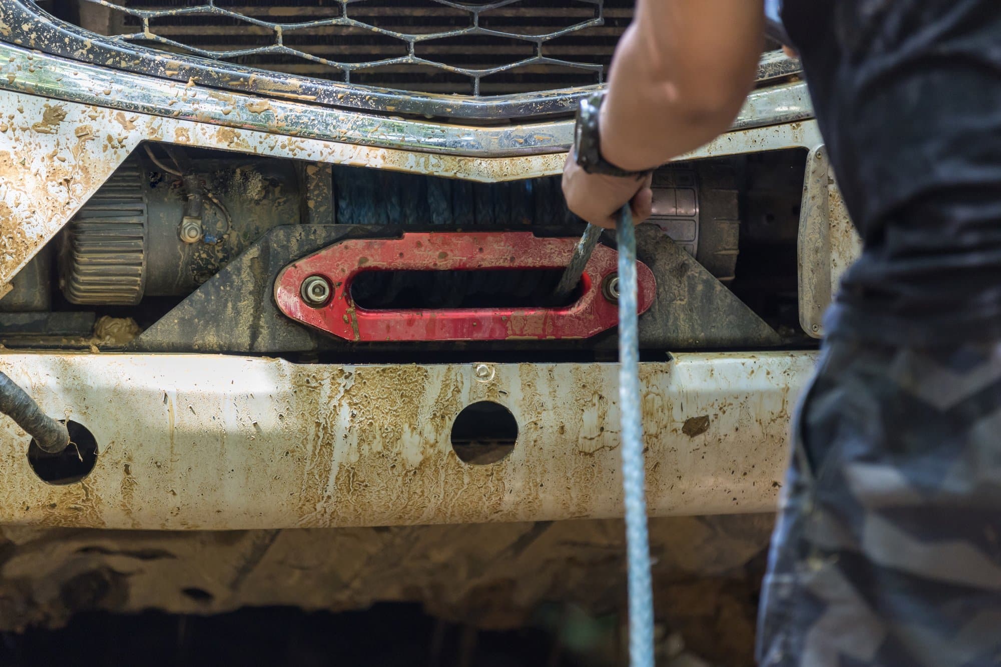 Driver pulling synthetic line off a bumper-mounted winch on a pickup