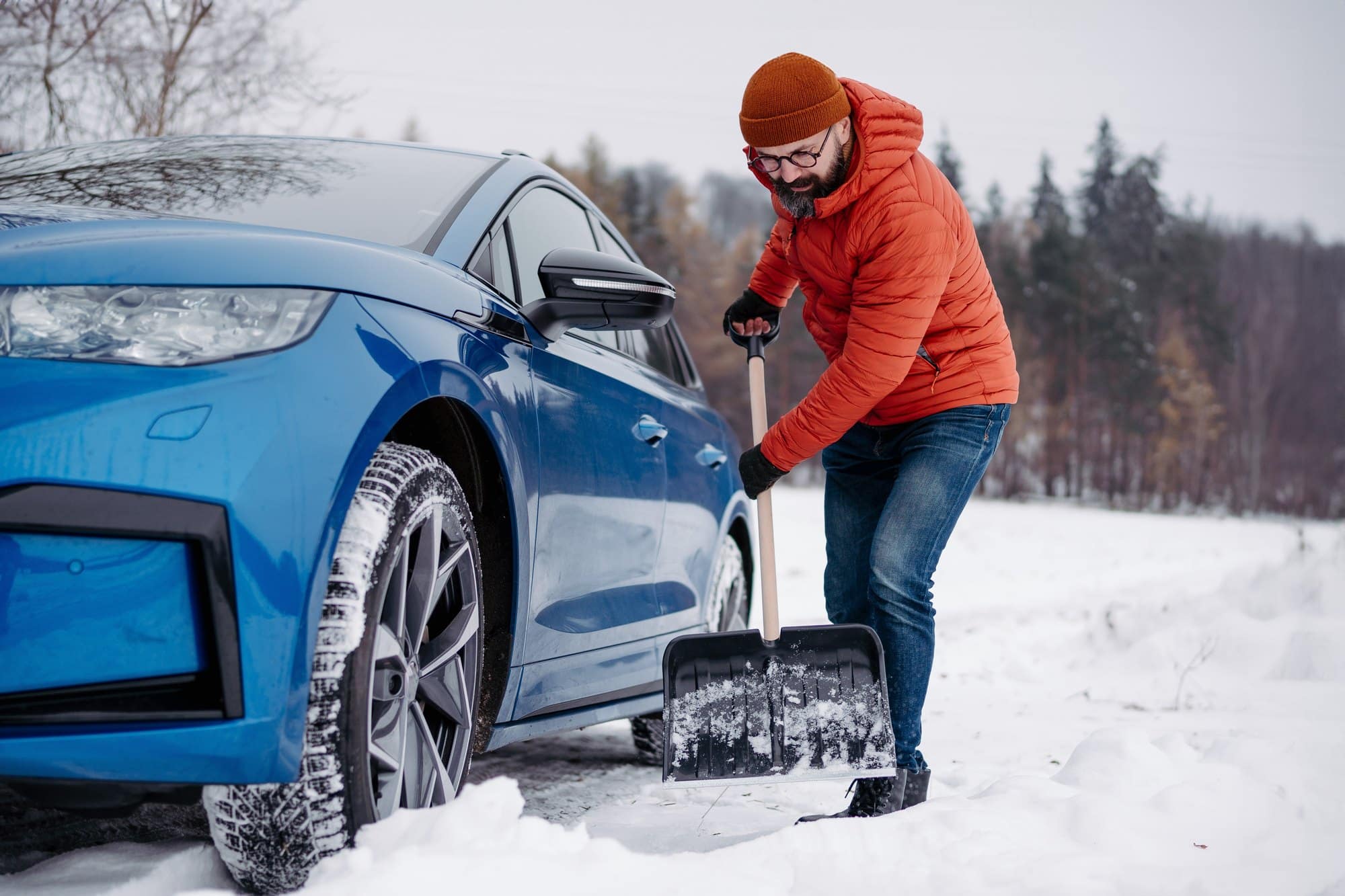 Shoveling out a car stuck in snow Driver using a steel shovel to dig snow away from the front wheel of a stuck car