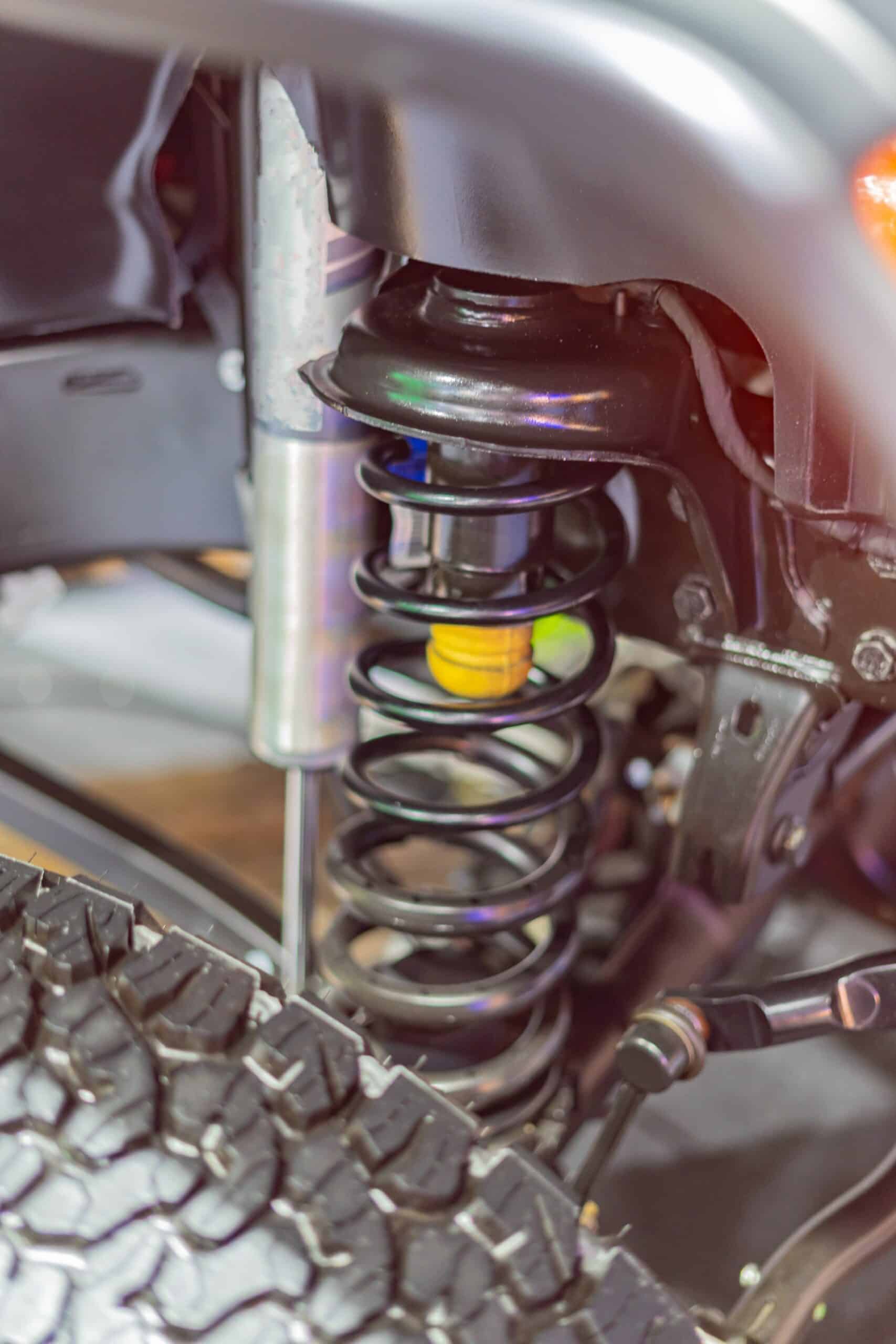 Off-road truck suspension shock close-up Close-up of an off-road truck shock absorber and coil spring above an all-terrain tire